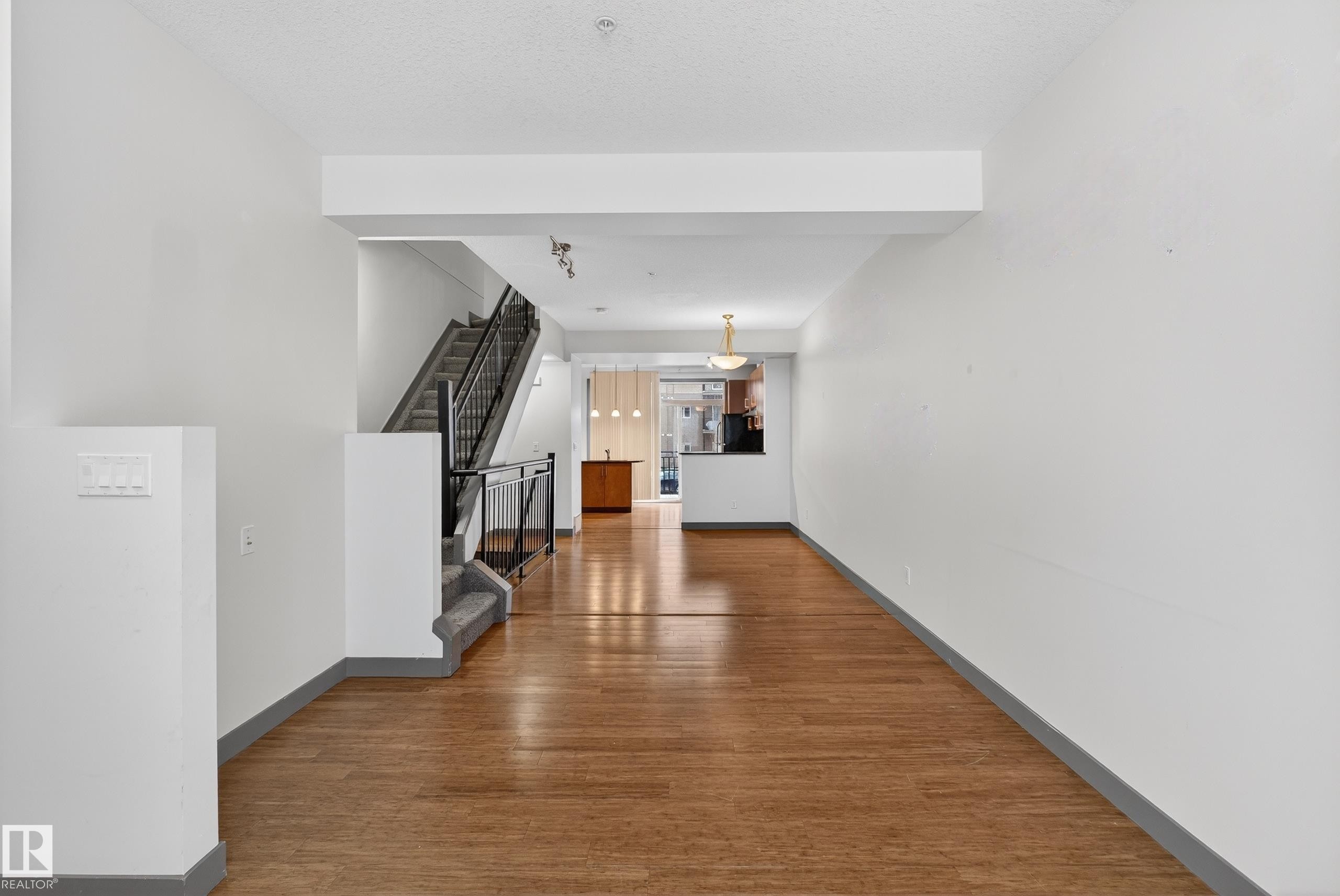 This expansive living area features hardwood flooring, white walls, and a staircase with dark railings - 1649 Cunningham Way, Edmonton, AB - Indoor Photo Showing Other Room
