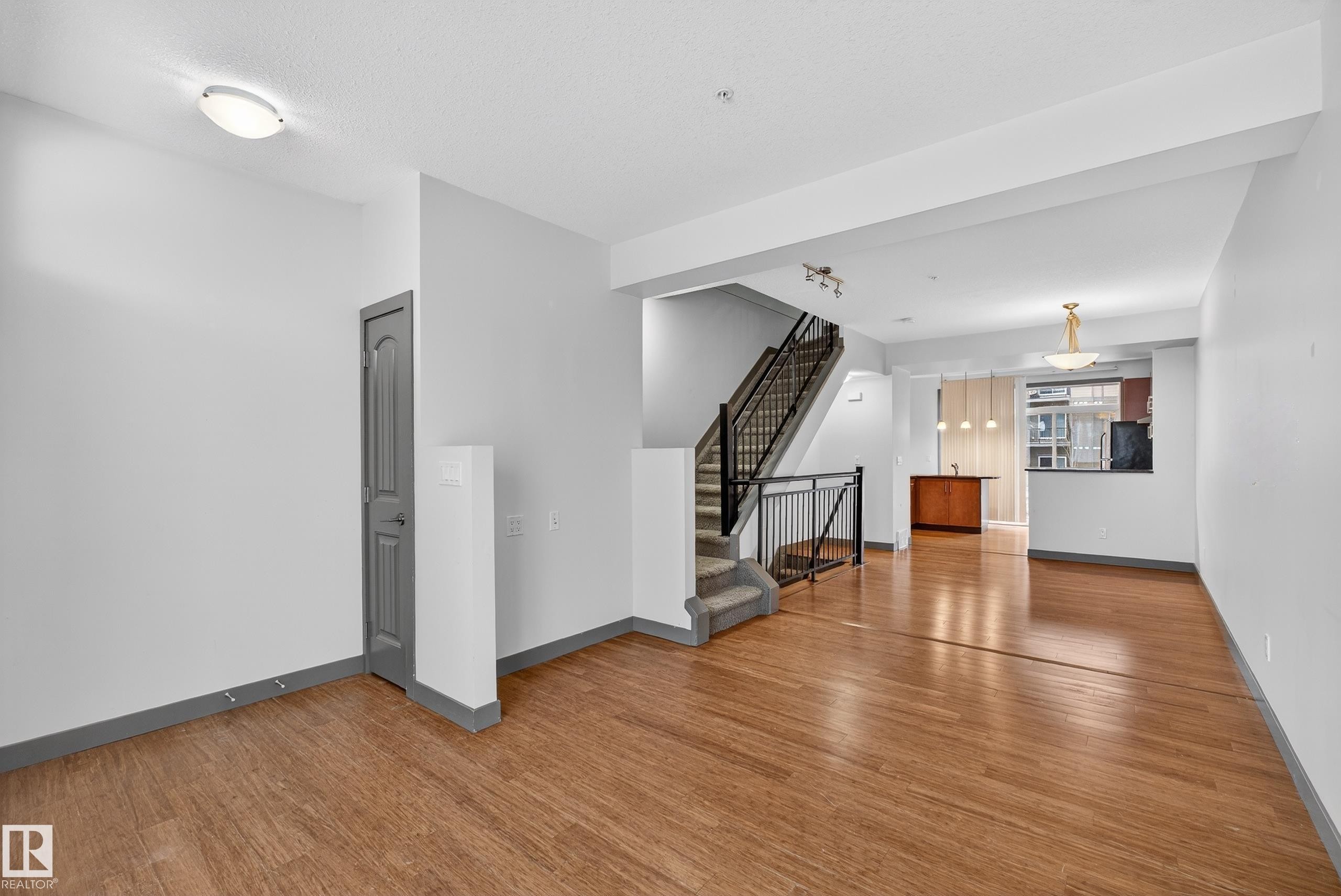 The property features hardwood floors, a staircase with dark railings, and light-colored walls - 1649 Cunningham Way, Edmonton, AB - Indoor Photo Showing Other Room