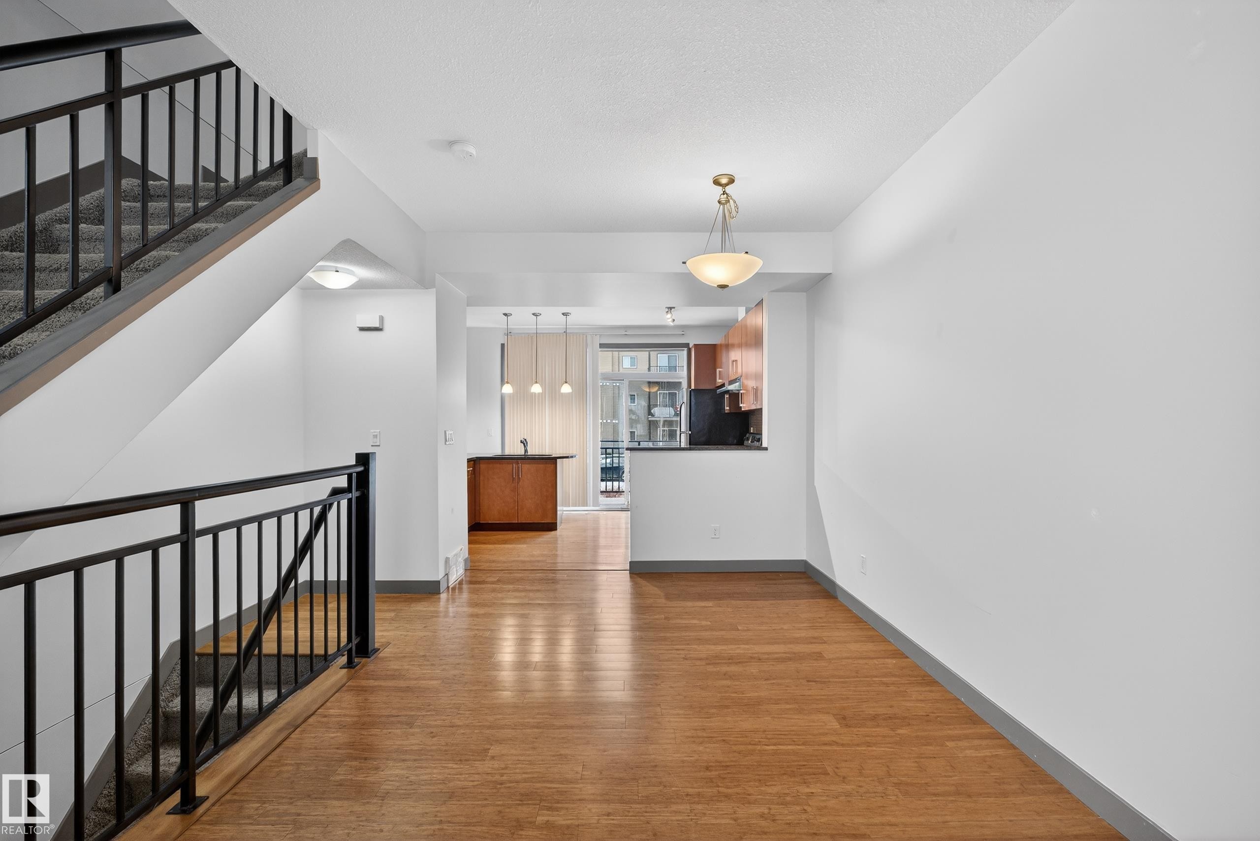Open concept living space featuring hardwood floors, a staircase with black metal railings, and a kitchen area with wood cabinetry and pendant lighting - 1649 Cunningham Way, Edmonton, AB - Indoor Photo Showing Other Room