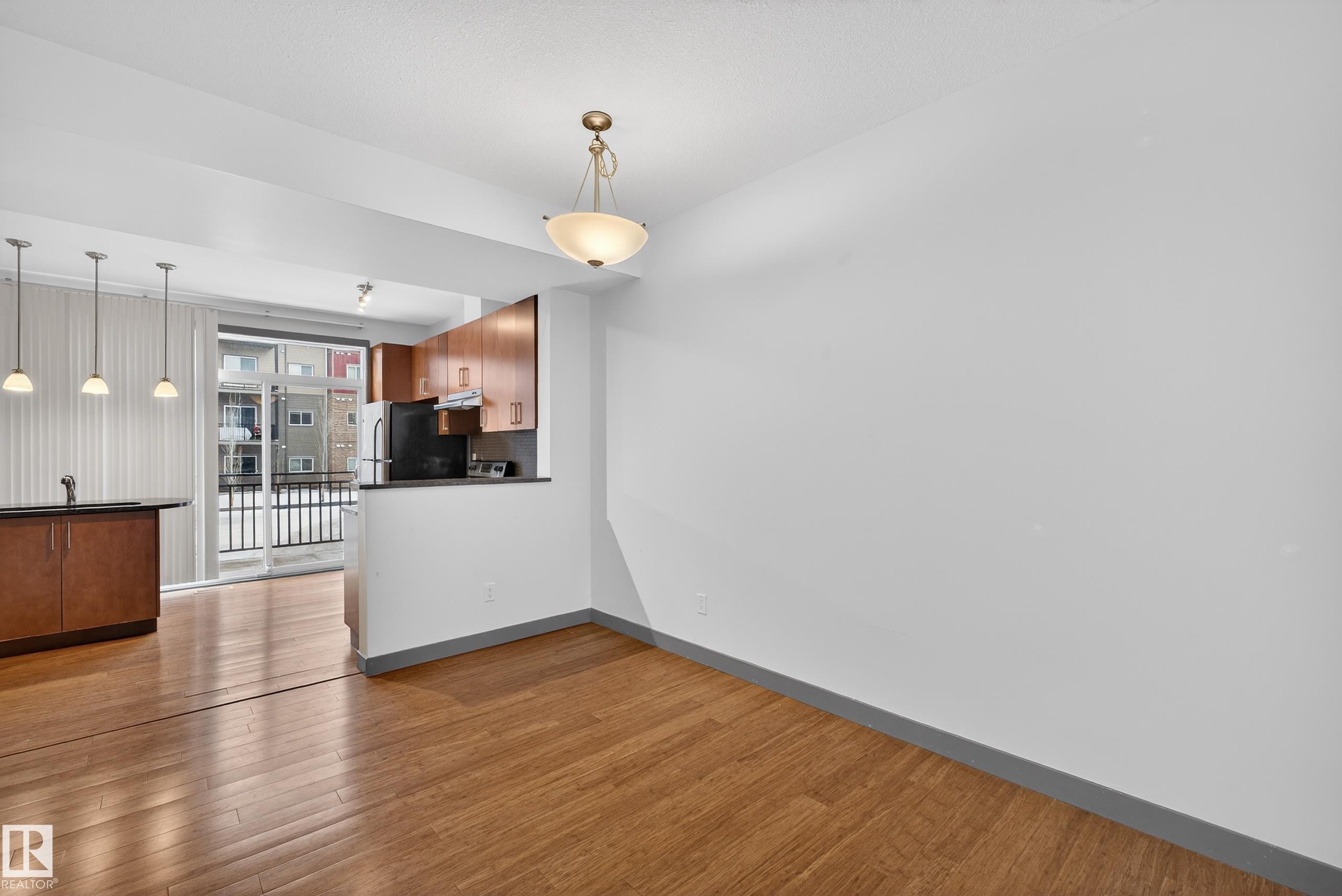 Open concept living space with hardwood floors, a kitchen area with wooden cabinetry, and a balcony with a black railing - 1649 Cunningham Way, Edmonton, AB - Indoor Photo Showing Other Room