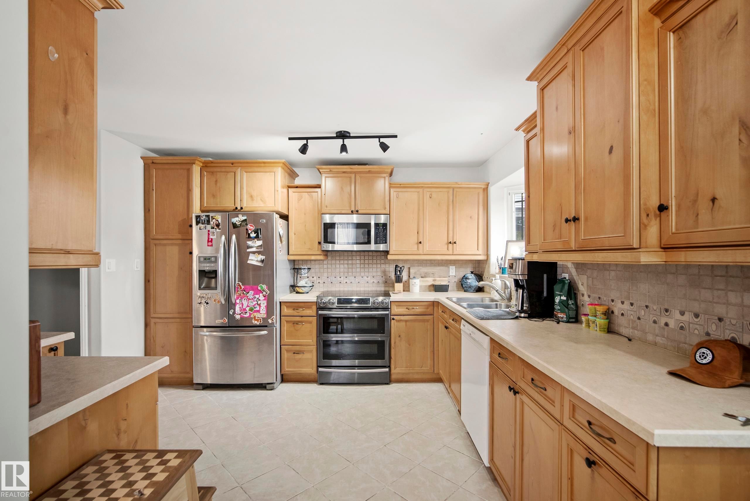 Kitchen with stainless steel appliances, light countertops, light tile patterned flooring, decorative backsplash, and track lighting - 9221 84 Street, Fort Saskatchewan, AB - Indoor Photo Showing Kitchen With Double Sink