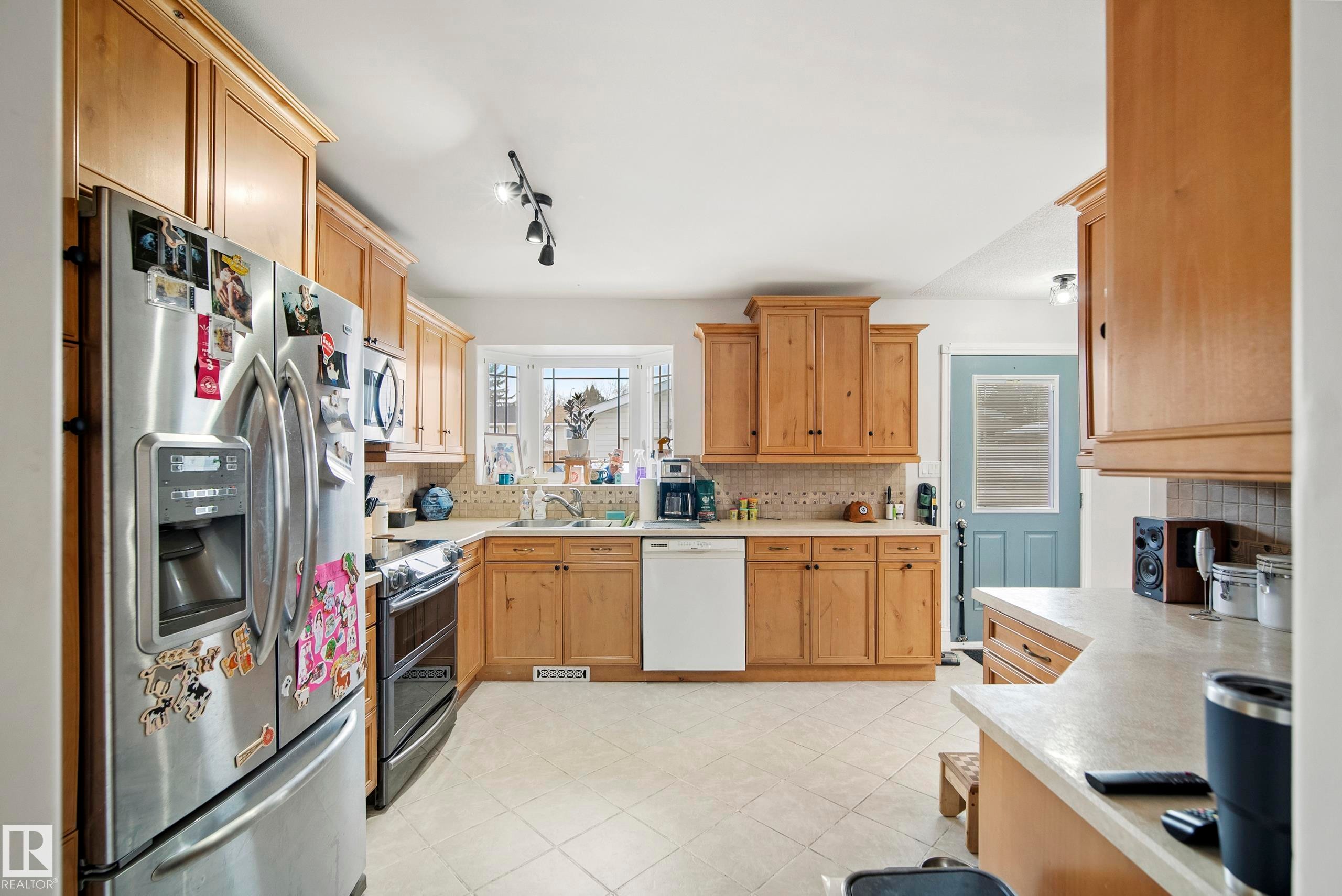 Kitchen featuring stainless steel appliances, light countertops, decorative backsplash, track lighting, and light tile patterned floors - 9221 84 Street, Fort Saskatchewan, AB - Indoor Photo Showing Kitchen With Double Sink