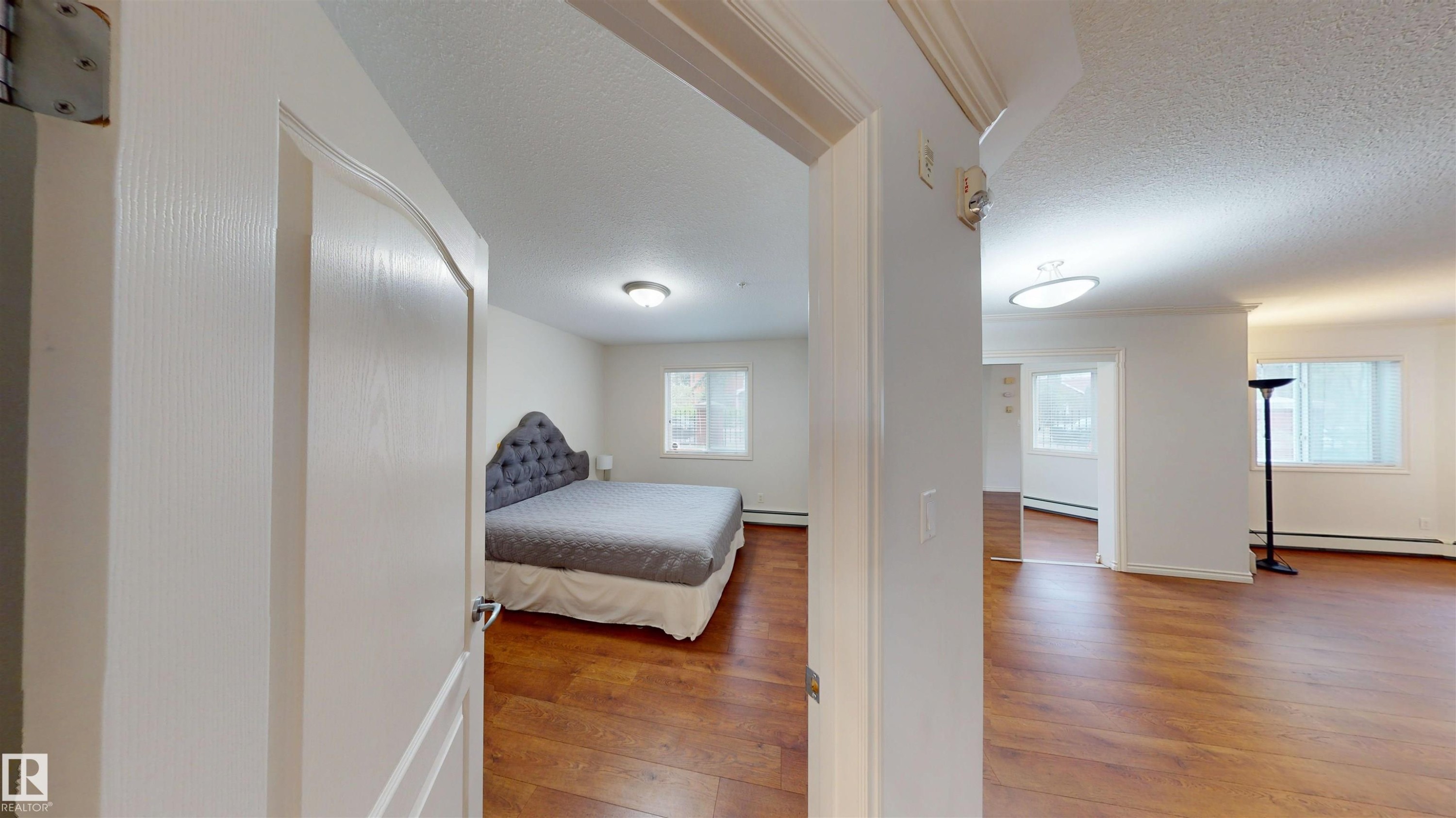 Bedroom with light wood finished floors, a textured ceiling, and a baseboard heating unit - 115 9938 104 St, Edmonton, AB - Indoor Photo Showing Other Room