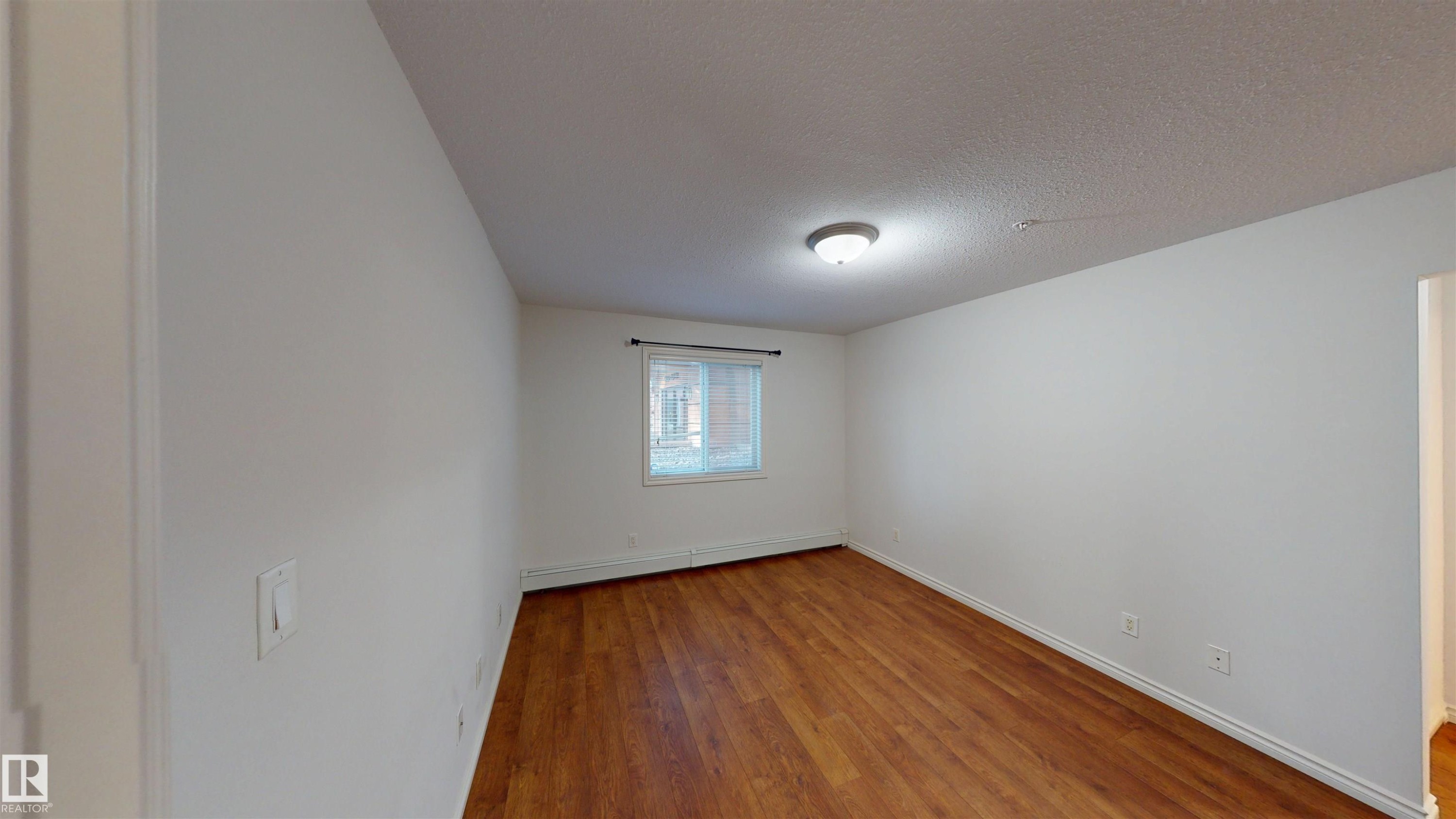 Empty room featuring light wood-type flooring, a textured ceiling, and a baseboard radiator - 115 9938 104 St, Edmonton, AB - Indoor Photo Showing Other Room