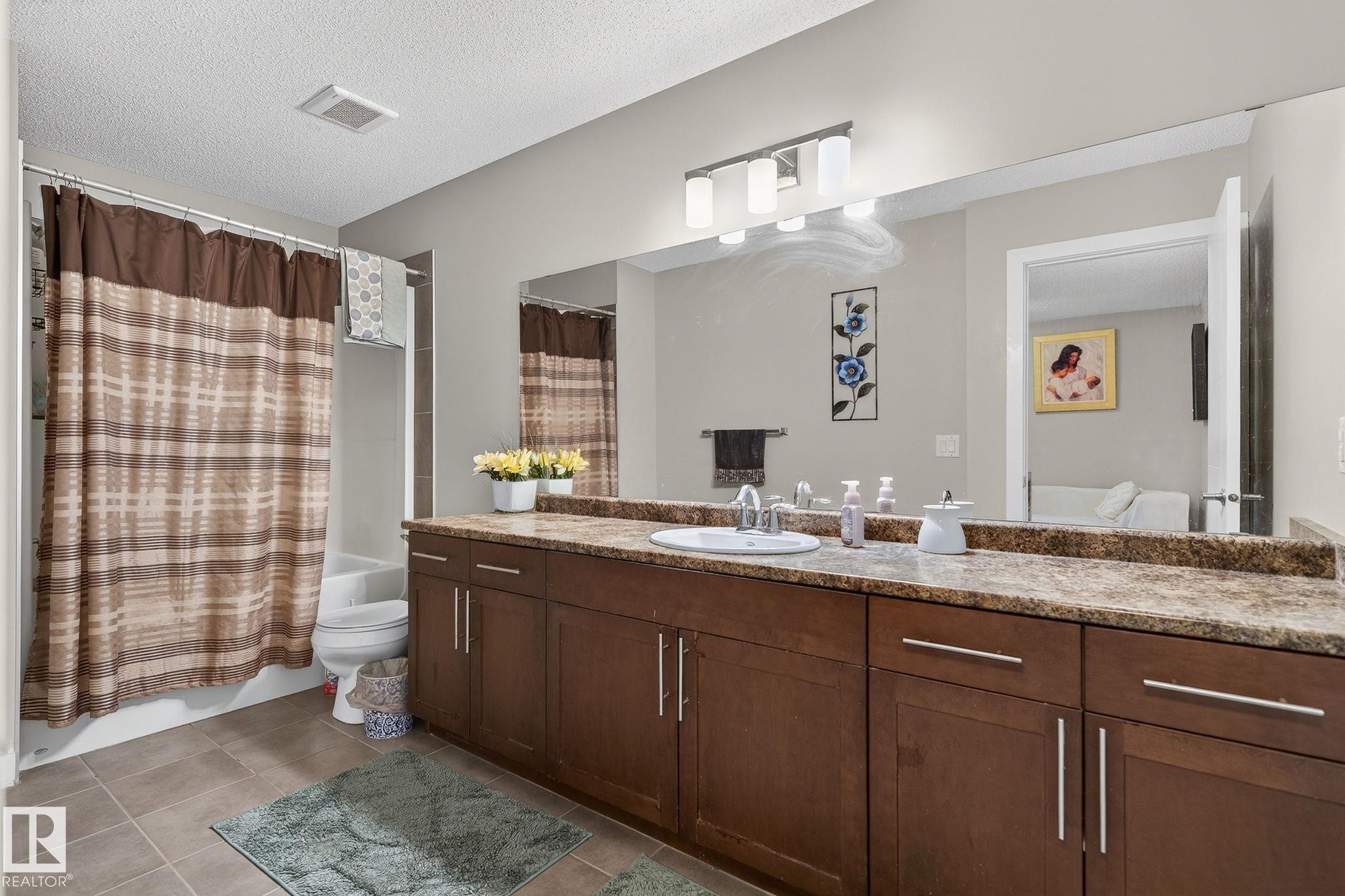 Bathroom featuring vanity, shower / bath combo, a textured ceiling, and light tile patterned flooring - 21867 80 Avenue, Edmonton, AB - Indoor Photo Showing Bathroom