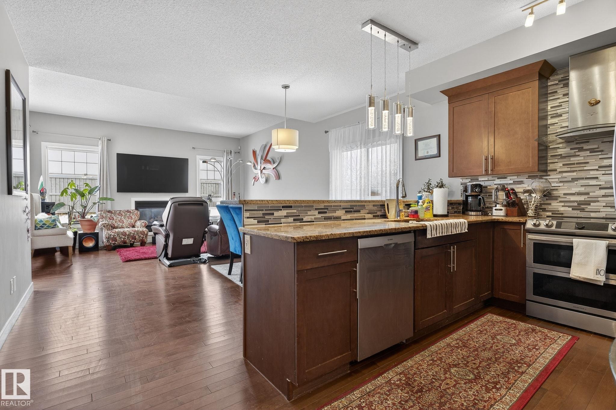 Kitchen featuring a peninsula, backsplash, stainless steel appliances, open floor plan, and a textured ceiling - 21867 80 Avenue, Edmonton, AB - Indoor Photo Showing Kitchen With Upgraded Kitchen
