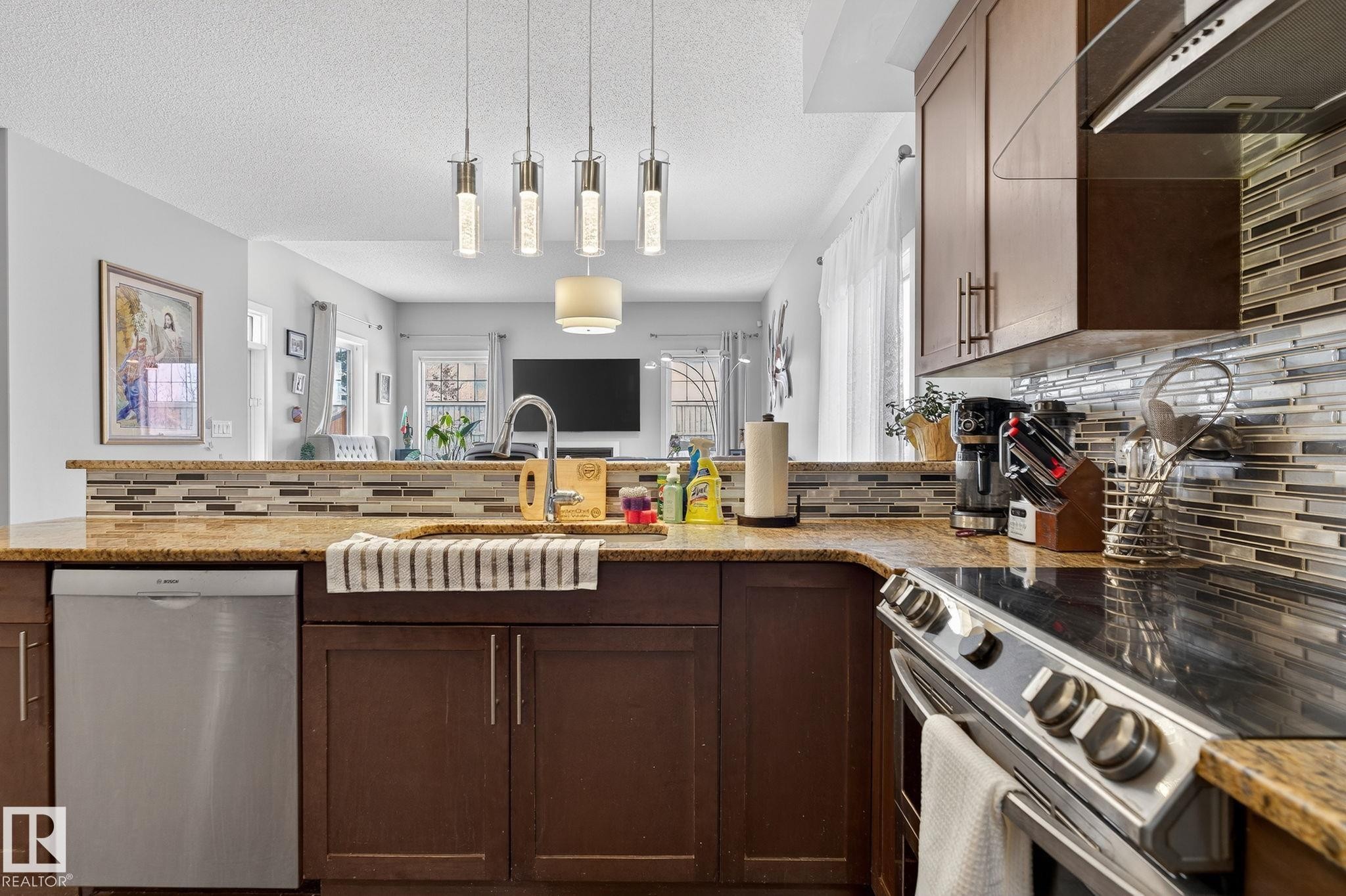 Kitchen featuring stainless steel appliances, a peninsula, decorative backsplash, extractor fan, and light stone counters - 21867 80 Avenue, Edmonton, AB - Indoor Photo Showing Kitchen