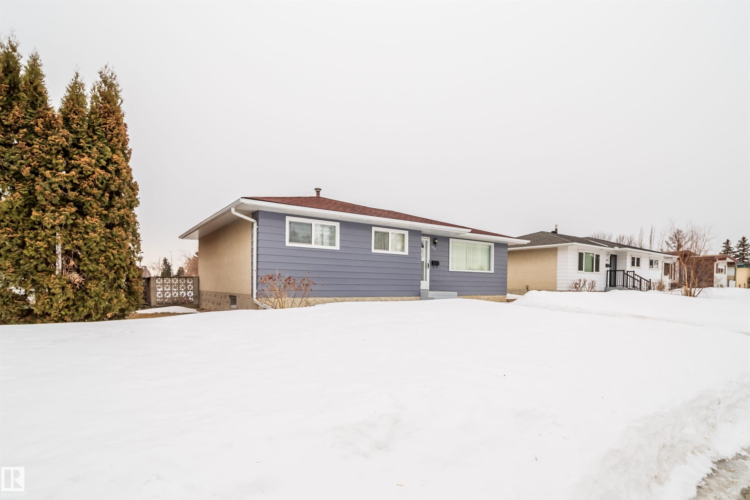 The property features a ranch-style house with blue siding and a dark roof, complemented by white trim around the windows - 7911 145 Avenue Nw, Edmonton, AB - Outdoor