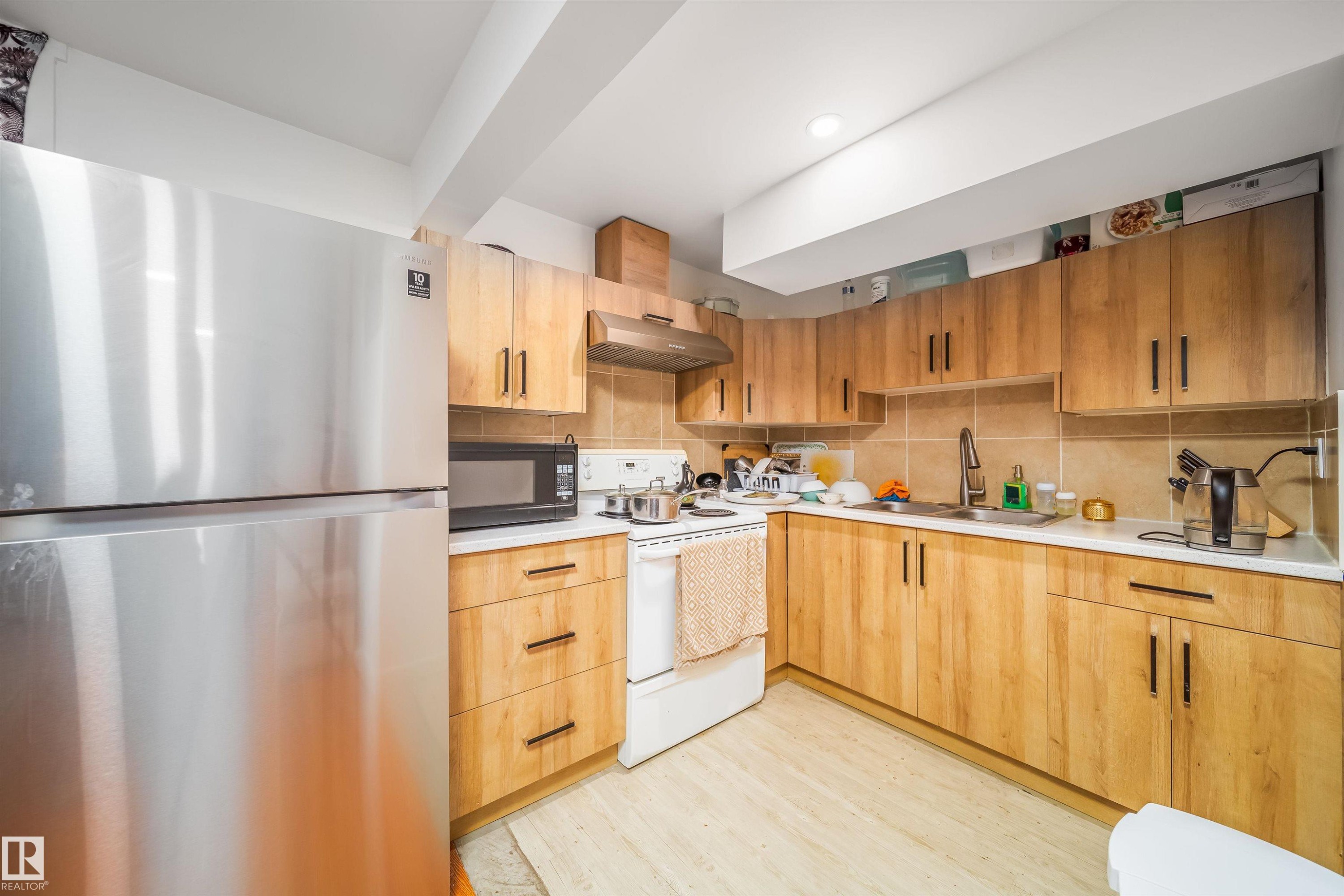 The kitchen features light wood cabinetry, a stainless steel refrigerator, and a light-colored tiled backsplash - 7911 145 Avenue Nw, Edmonton, AB - Indoor Photo Showing Kitchen