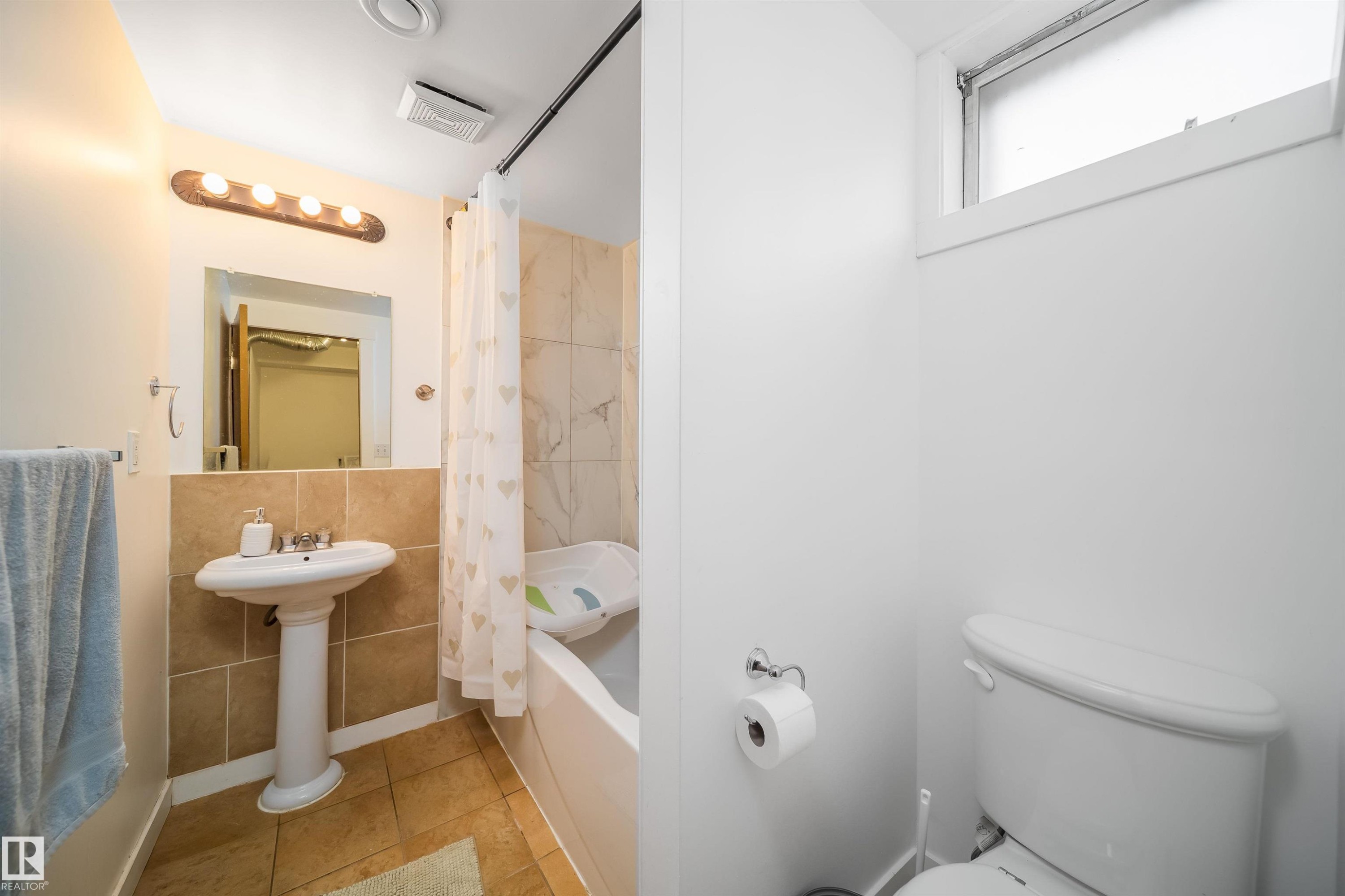 The bathroom features a pedestal sink, a tiled vanity backsplash, a bathtub with tiled surround, and a toilet - 7911 145 Avenue Nw, Edmonton, AB - Indoor Photo Showing Bathroom