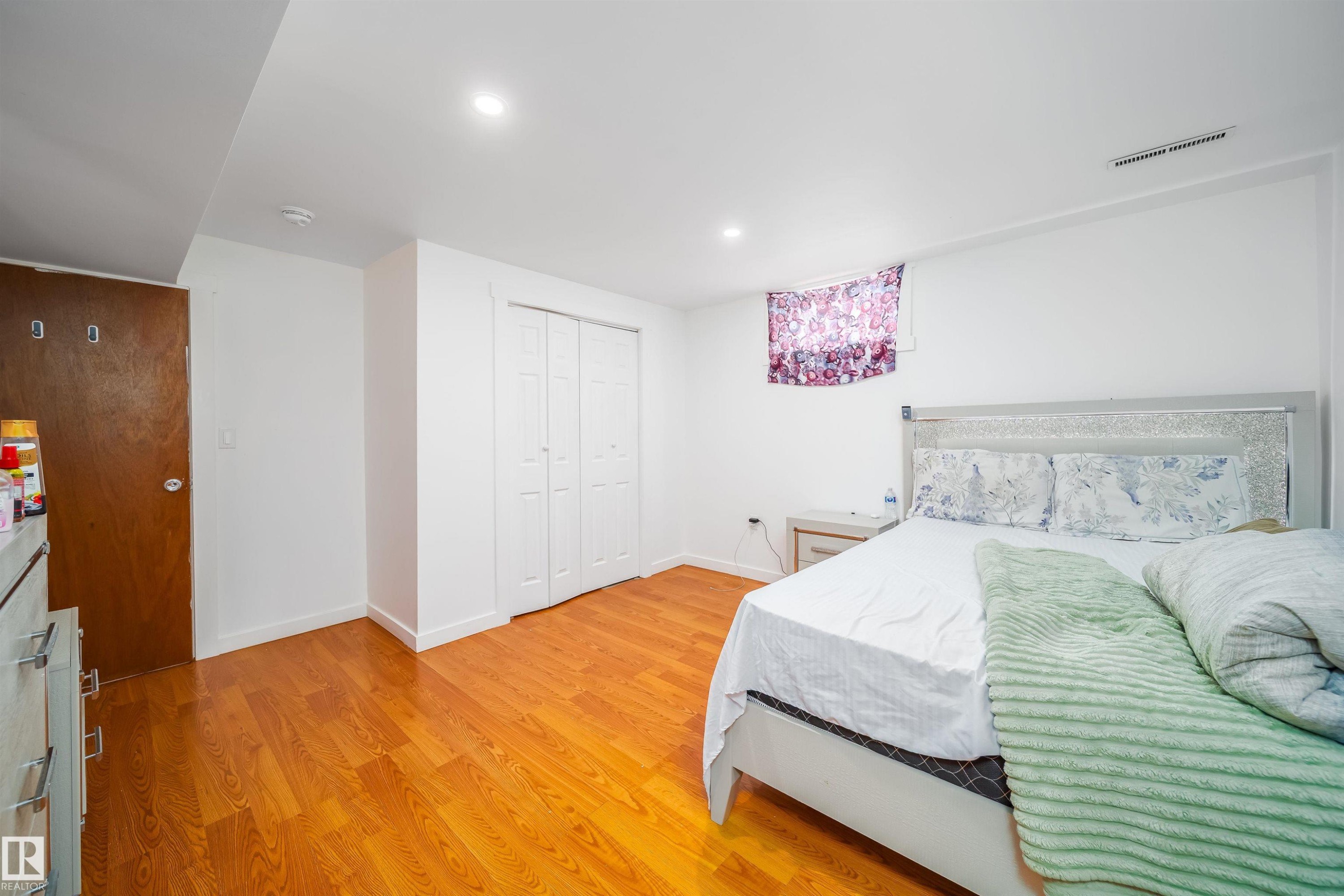 This room features hardwood floors, a white door with two white bi-fold closet doors, and white walls - 7911 145 Avenue Nw, Edmonton, AB - Indoor Photo Showing Bedroom