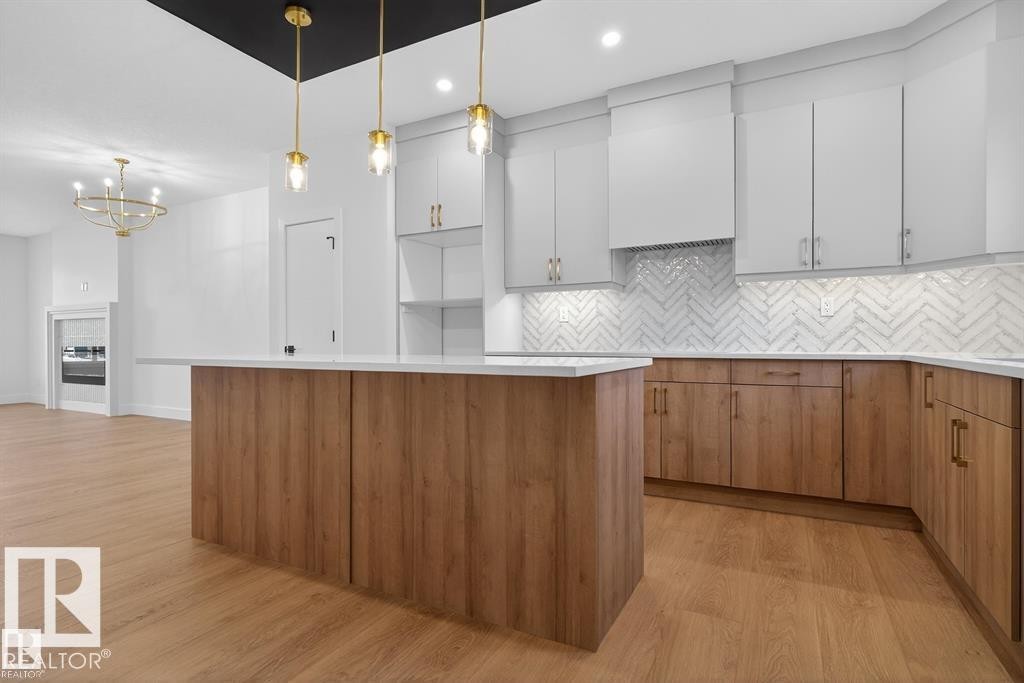 Kitchen featuring light wood-style floors, decorative backsplash, a center island, wood finish cabinetry, and suspended lighting - 45 Rosa Crescent, St. Albert, AB - Indoor Photo Showing Kitchen