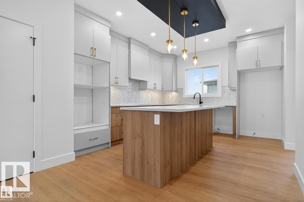 Two tone kitchen with two tone color scheme, a kitchen island, light countertops, light wood-type flooring, and tasteful backsplash - 45 Rosa Crescent, St. Albert, AB - Indoor Photo Showing Kitchen