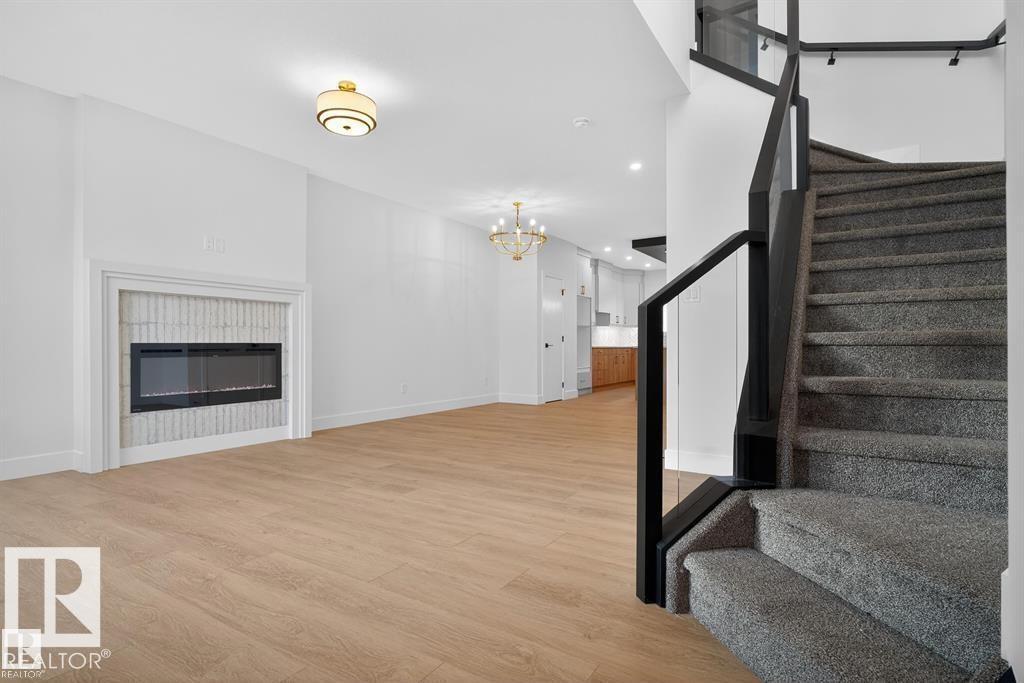 Staircase featuring wood finished floors, a glass covered fireplace, and hanging lights - 45 Rosa Crescent, St. Albert, AB - Indoor With Fireplace