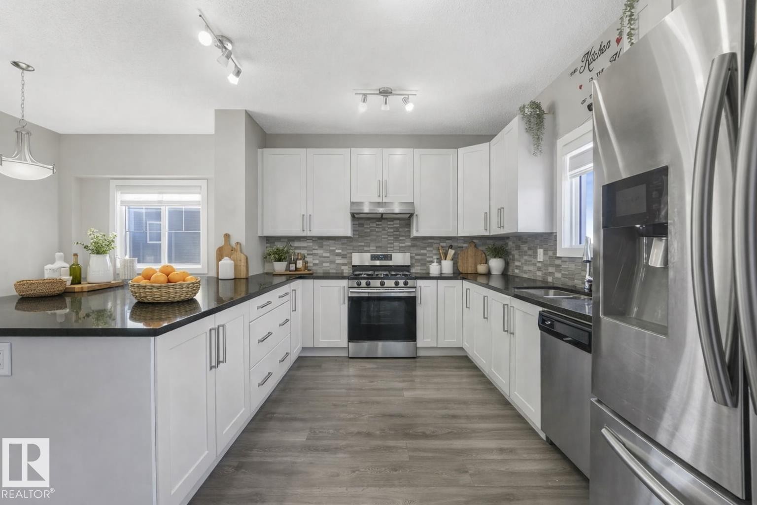 Kitchen with stainless steel appliances, a peninsula, dark stone countertops, decorative light fixtures, and white cabinets - 2428 Wonnacott Crest, Edmonton, AB - Indoor Photo Showing Kitchen With Upgraded Kitchen