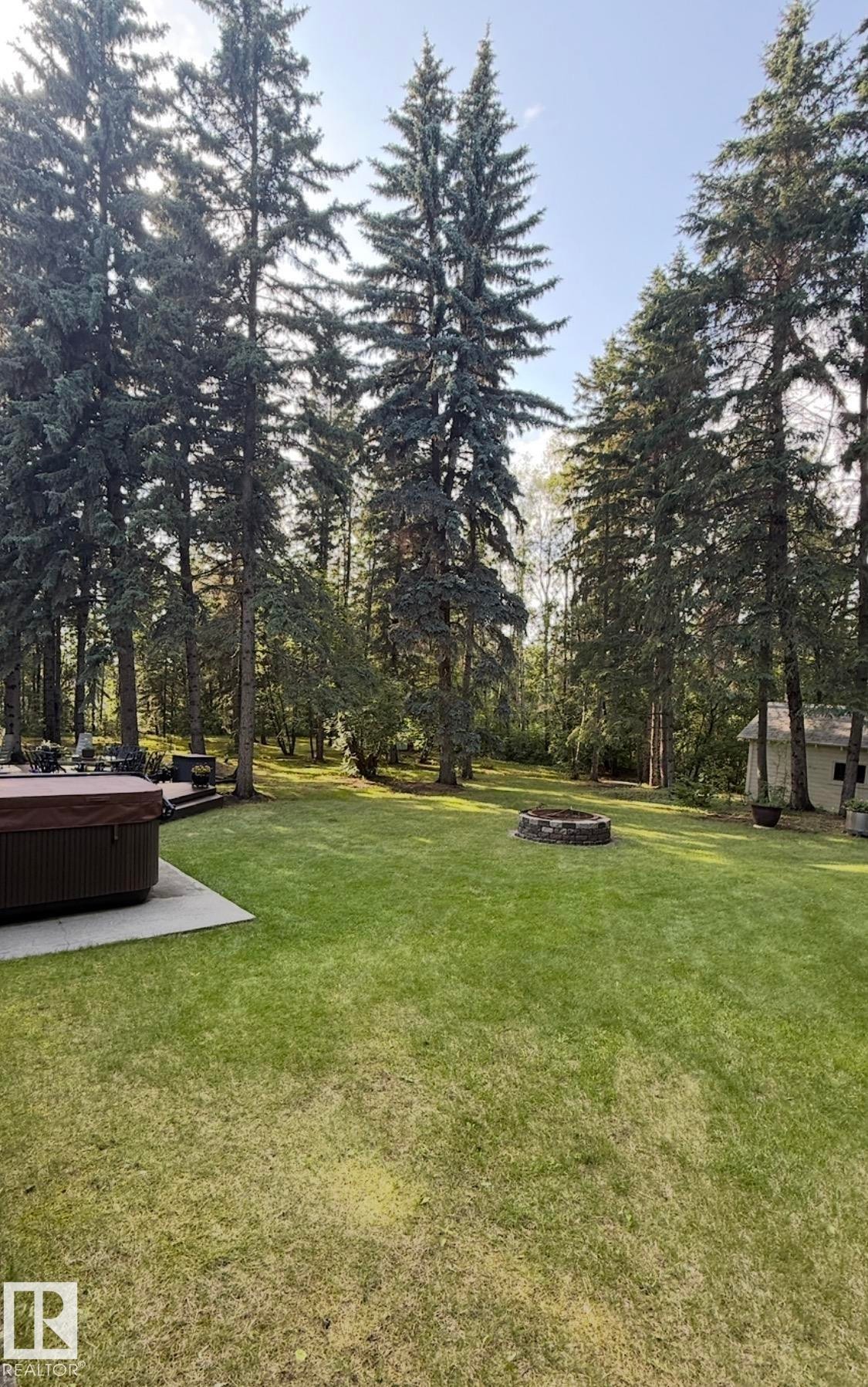 View of grassy yard with a patio area, a hot tub, a fire pit, and view of scattered trees - Edmonton, AB - Outdoor