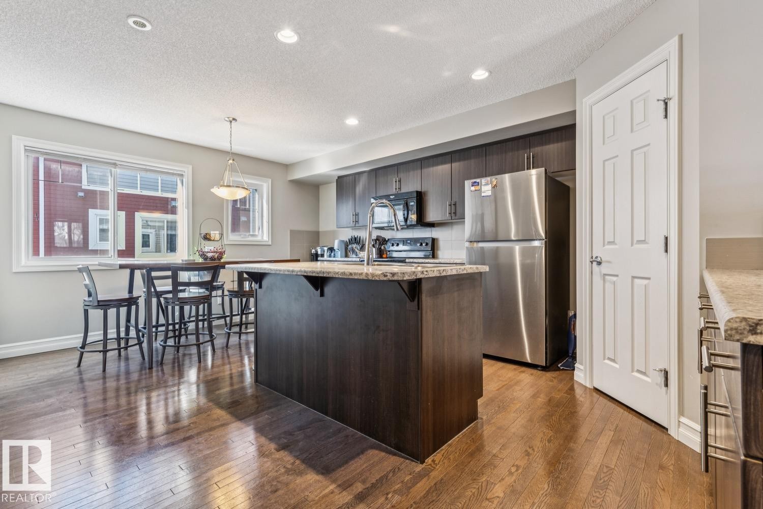 Kitchen featuring black appliances, a kitchen breakfast bar, light stone countertops, a center island with sink, and dark wood finished floors - 5409 3 Avenue, Edmonton, AB - Indoor Photo Showing Kitchen