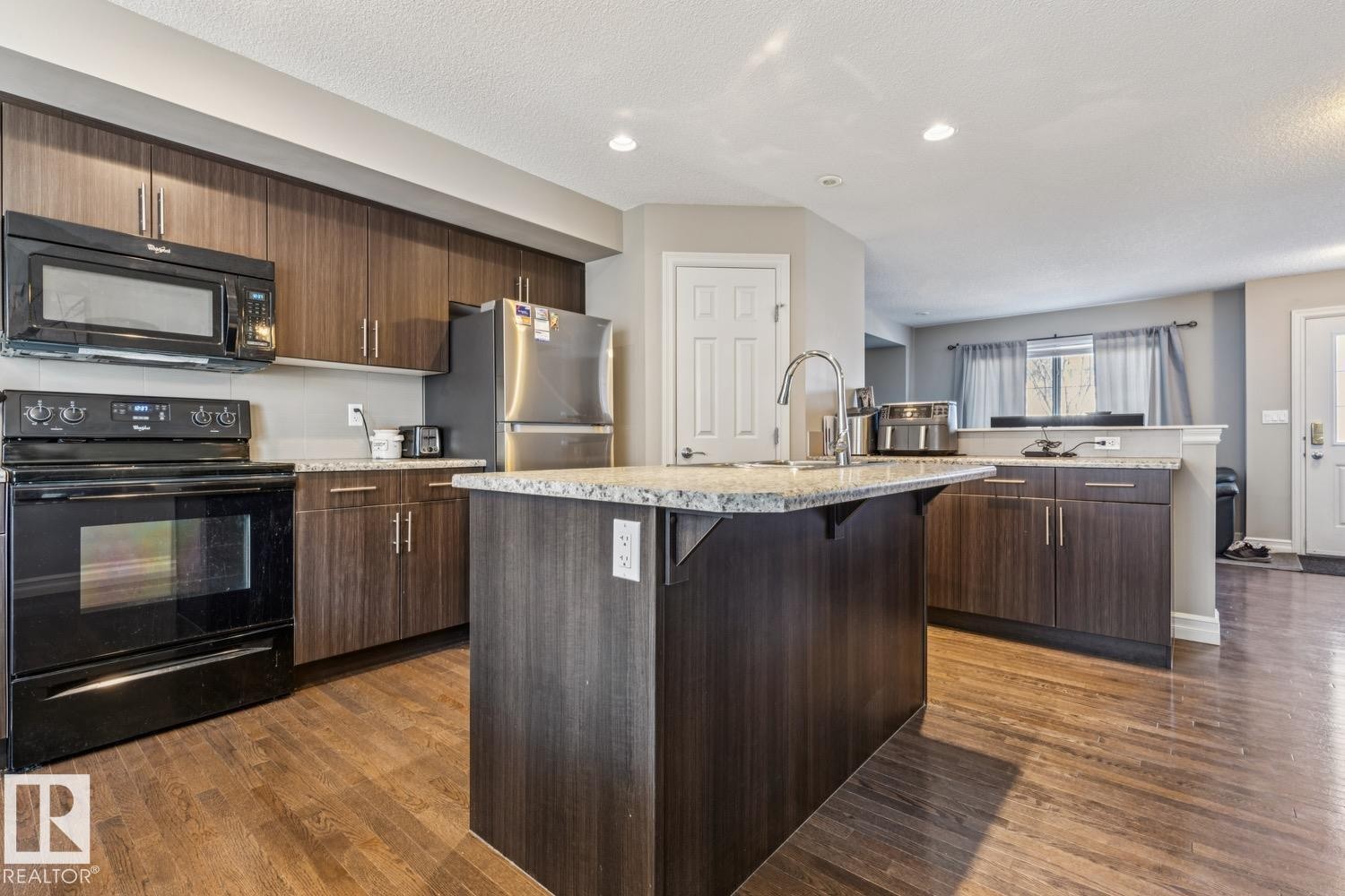 Kitchen with black appliances, a breakfast bar, an island with sink, dark wood finished floors, and dark wood finish cabinetry - 5409 3 Avenue, Edmonton, AB - Indoor Photo Showing Kitchen