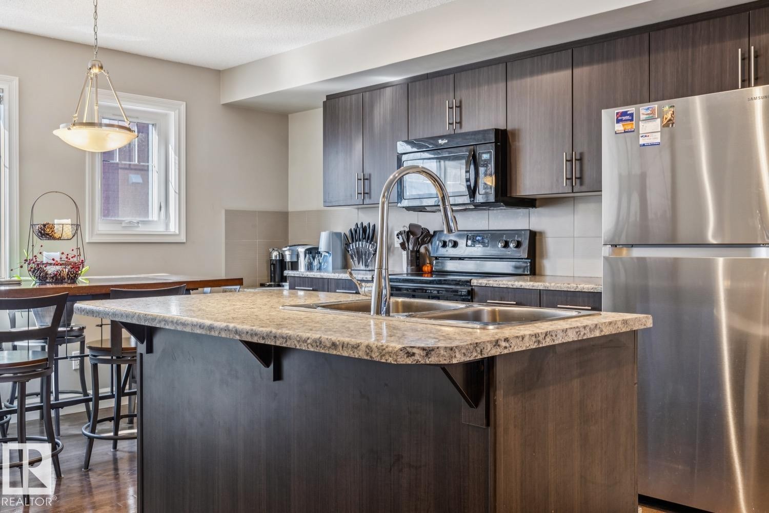 Kitchen with freestanding refrigerator, dark wood finish cabinets, a breakfast bar area, a kitchen island with sink, and tasteful backsplash - 5409 3 Avenue, Edmonton, AB - Indoor Photo Showing Kitchen With Double Sink With Upgraded Kitchen