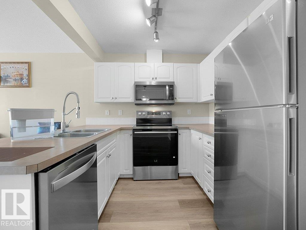 Kitchen featuring stainless steel appliances, white cabinets, rail lighting, light wood-type flooring, and a peninsula - 196 230 Edwards Drive, Edmonton, AB - Indoor Photo Showing Kitchen With Double Sink