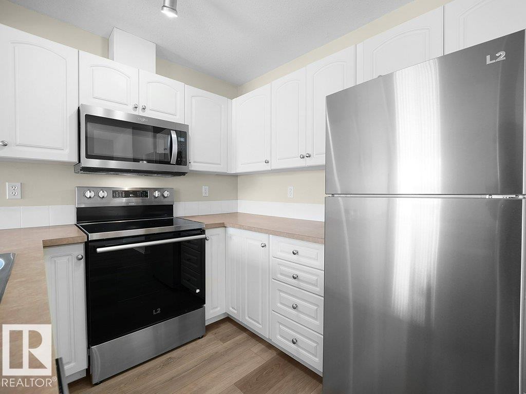 Kitchen with stainless steel appliances, white cabinets, light countertops, light wood-type flooring, and rail lighting - 196 230 Edwards Drive, Edmonton, AB - Indoor Photo Showing Kitchen