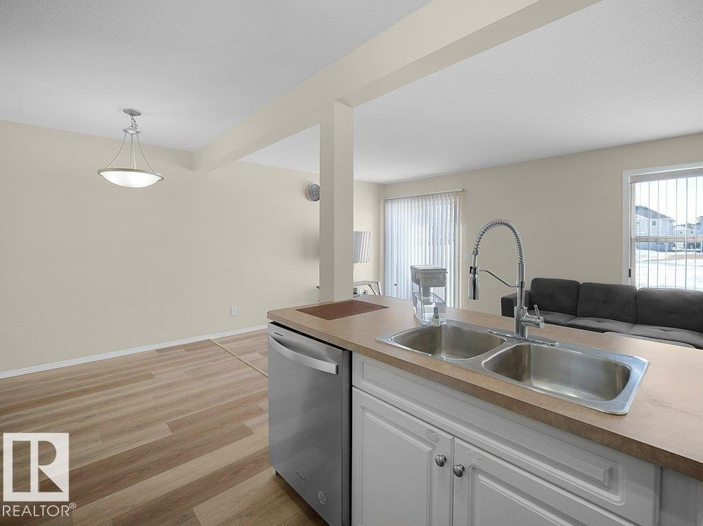 Kitchen with open floor plan, stainless steel dishwasher, white cabinets, light wood-style flooring, and light countertops - 196 230 Edwards Drive, Edmonton, AB - Indoor Photo Showing Kitchen With Double Sink