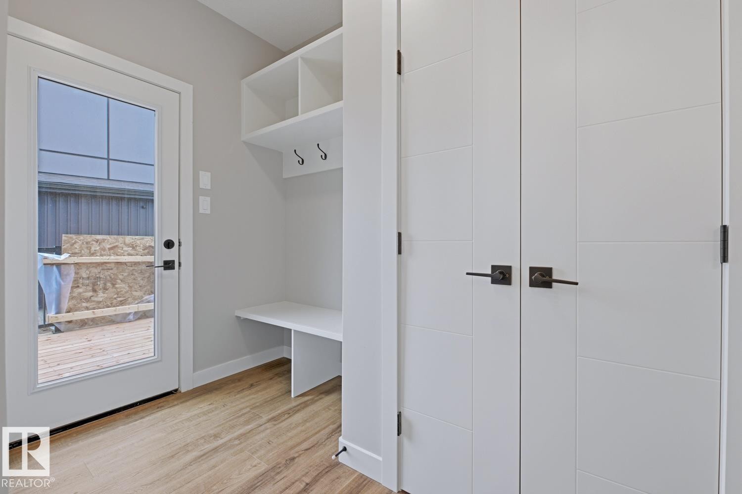 Entryway featuring wood-finish flooring, a white built-in storage bench with shelving and hooks, and a glass-paned door with dark hardware - 30 Chartres Close Nw, St. Albert, AB