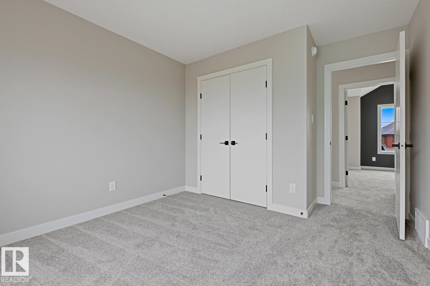 Light gray wall color with white trim, soft gray carpeting, and a white bi-fold closet with matte black hardware - 30 Chartres Close Nw, St. Albert, AB