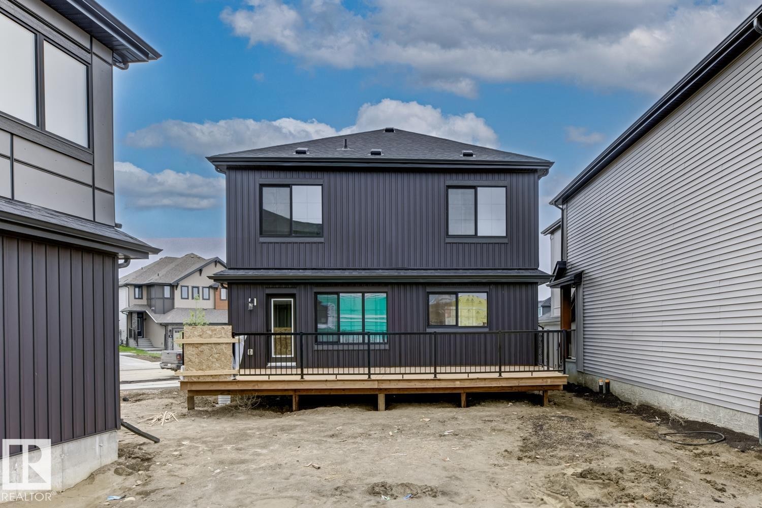 Two-story residence featuring a dark vertical siding exterior and a rear wooden deck with black railings - 30 Chartres Close Nw, St. Albert, AB
