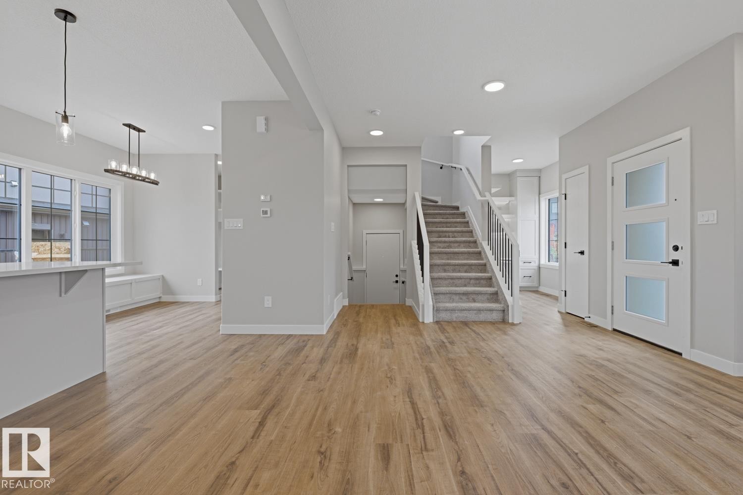 Spacious entry foyer featuring wood-finish flooring, a contemporary staircase with carpeted treads and metal balusters, recessed lighting, and a modern entry door with frosted glass panels - 30 Chartres Close Nw, St. Albert, AB