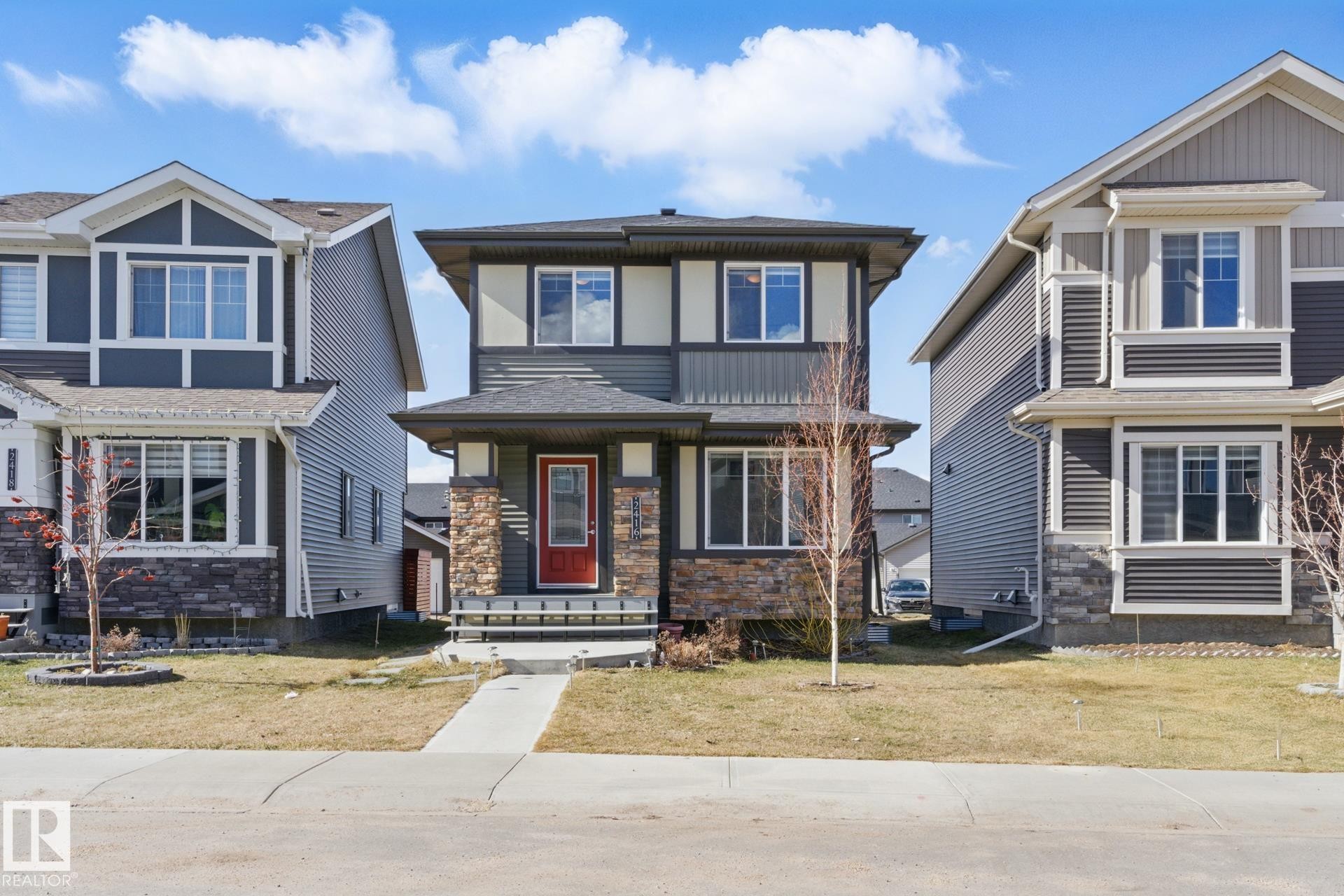 The property features a two-story exterior with a red front door, stone accents, and varied siding - 2416 Wonnacott Crest Sw, Edmonton, AB - Outdoor With Facade