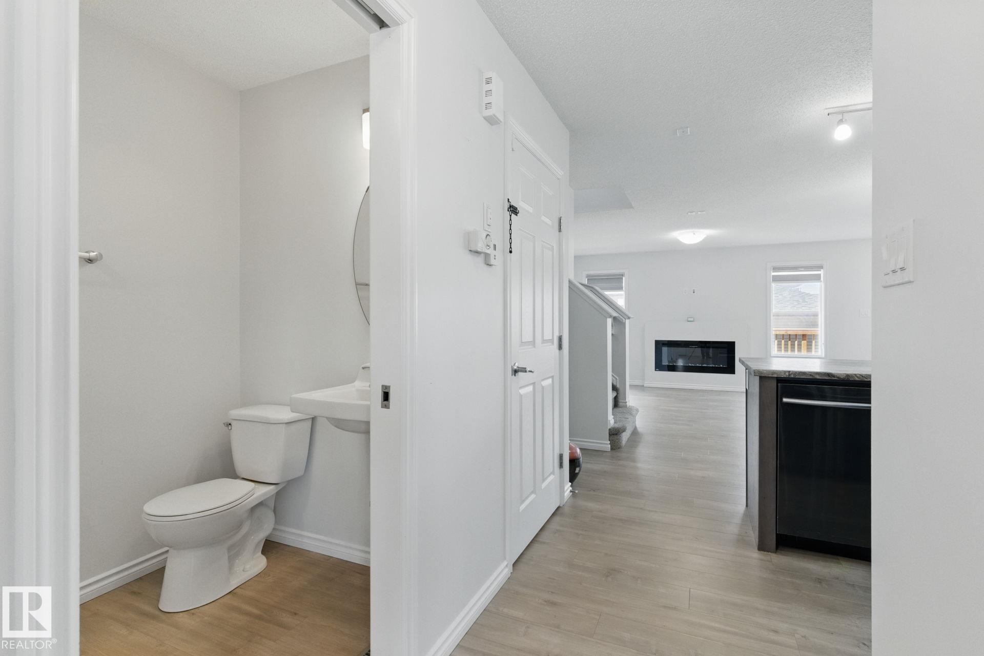The property features a powder room with a white toilet and pedestal sink, complemented by a round mirror - 2416 Wonnacott Crest Sw, Edmonton, AB - Indoor Photo Showing Bathroom