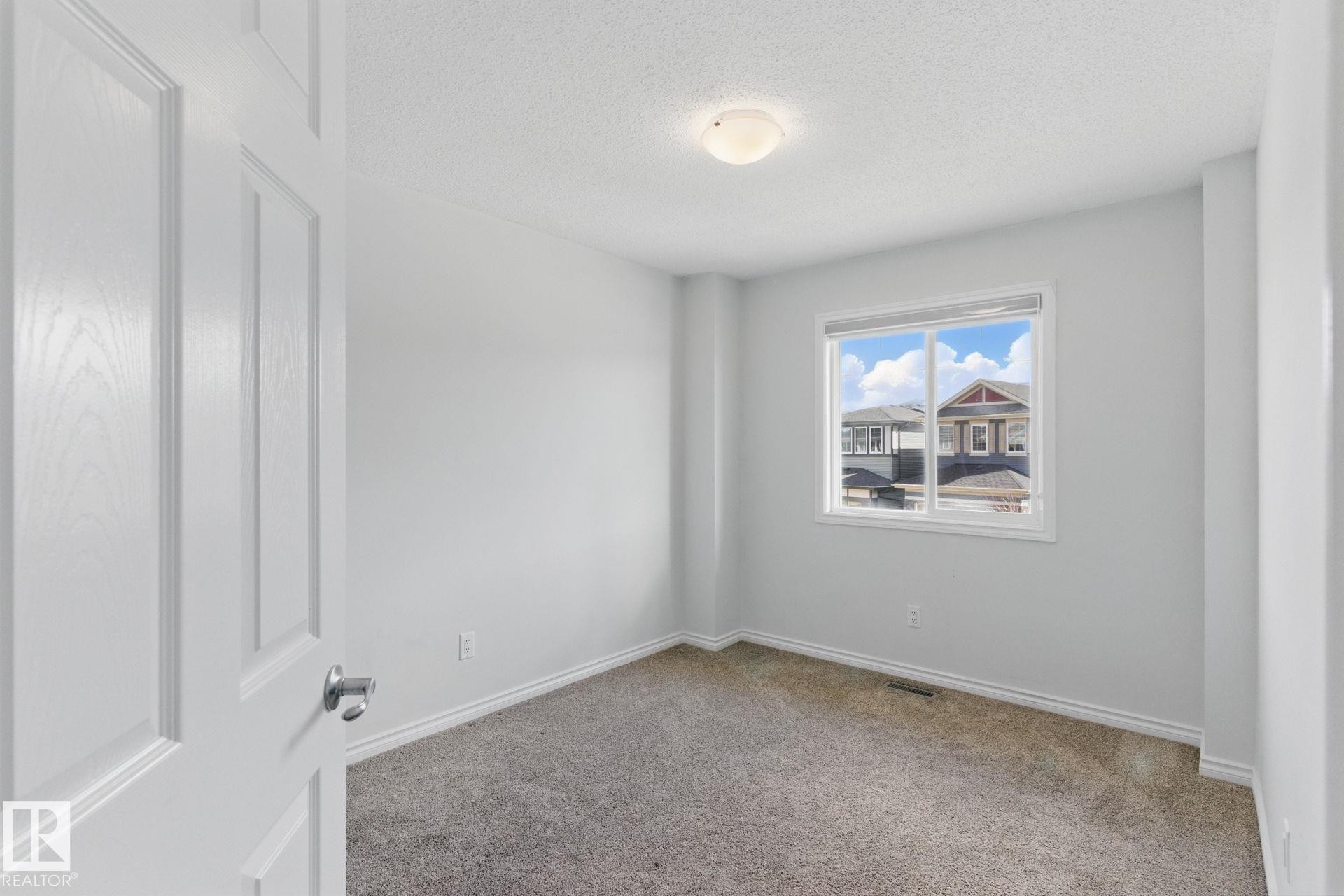 This room features neutral-toned carpet, light gray walls, white trim, and a window providing natural light - 2416 Wonnacott Crest Sw, Edmonton, AB - Indoor Photo Showing Other Room