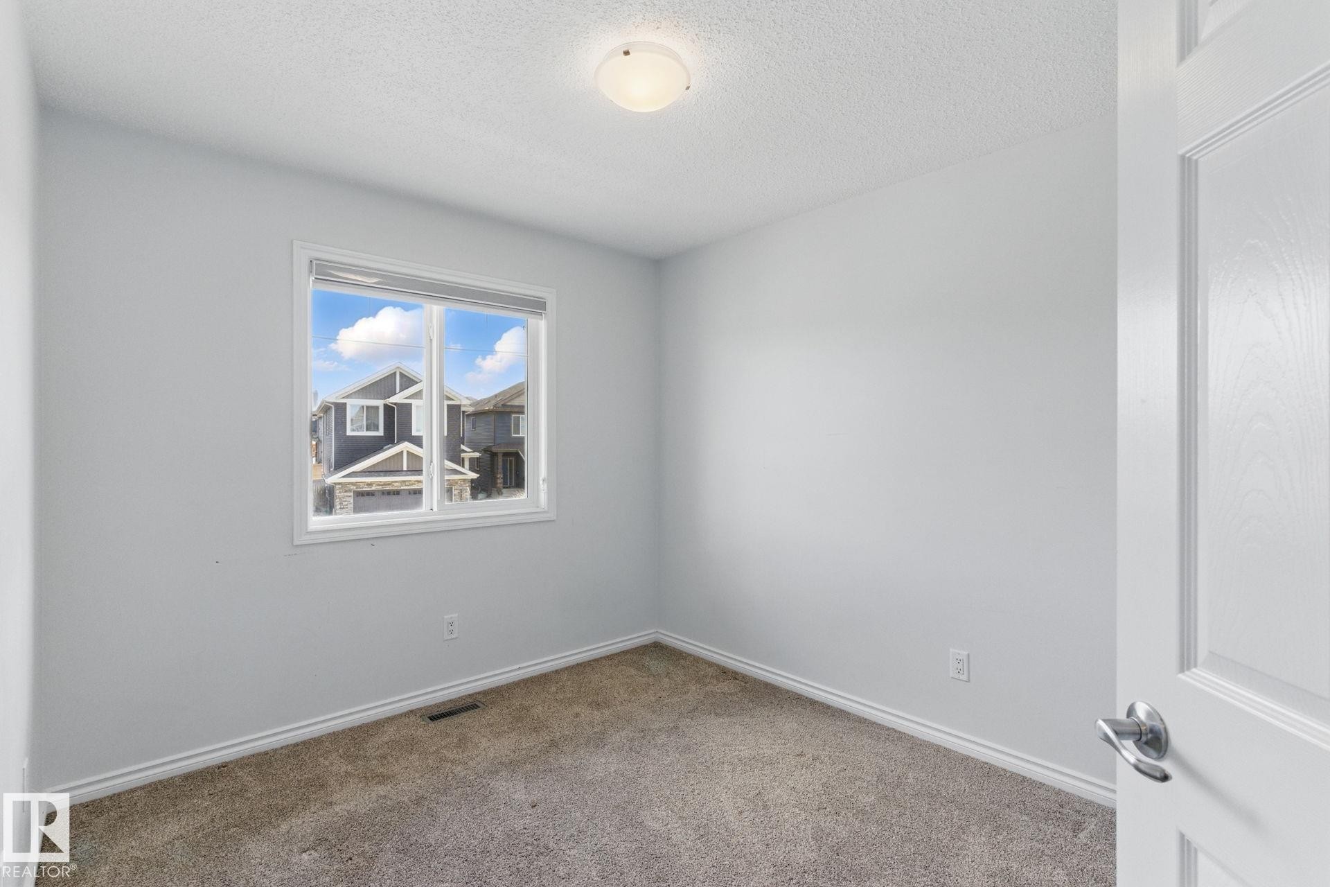 This room features neutral-toned walls, a window with a view of other properties and blue sky, and carpeted flooring - 2416 Wonnacott Crest Sw, Edmonton, AB - Indoor Photo Showing Other Room