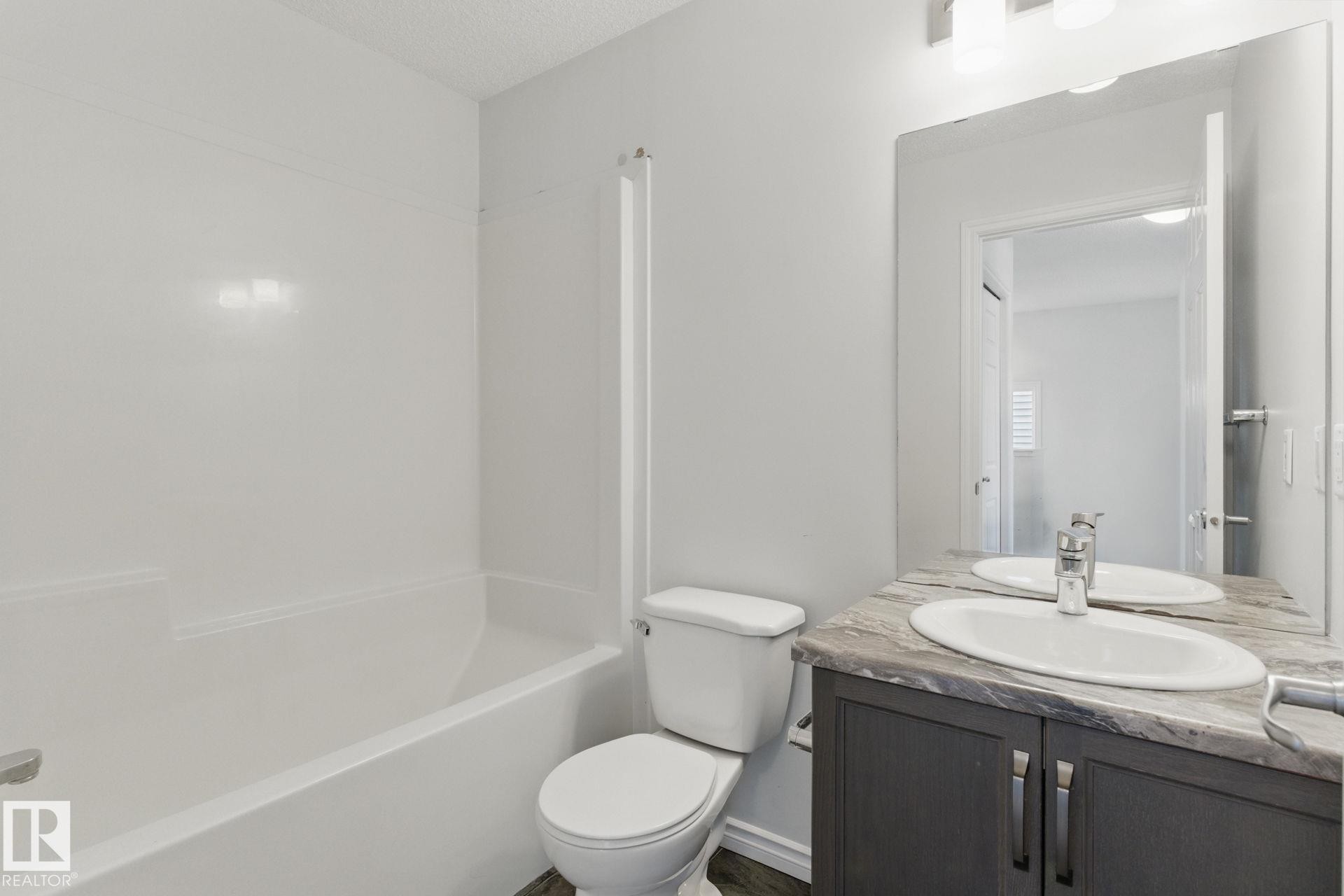 Bathroom featuring a white bathtub and shower surround, a toilet, and a vanity with a sink, faucet, and mirror - 2416 Wonnacott Crest Sw, Edmonton, AB - Indoor Photo Showing Bathroom