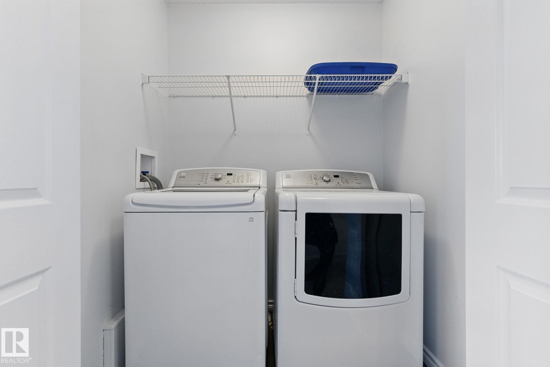 Dedicated laundry area featuring a white washing machine, a white dryer, and an overhead wire shelf - 2416 Wonnacott Crest Sw, Edmonton, AB - Indoor Photo Showing Laundry Room