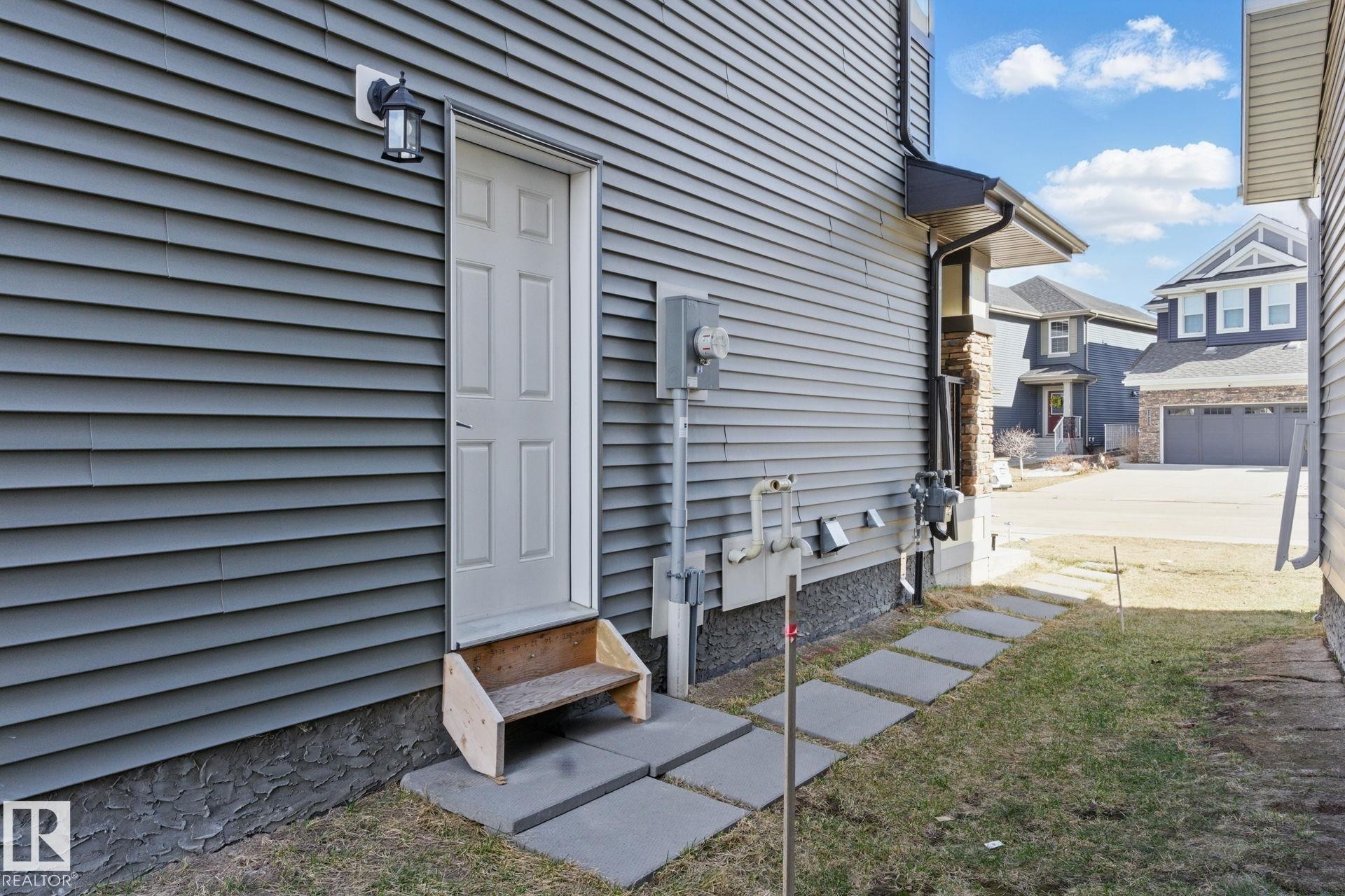The property features gray siding, a white exterior door, and a wall-mounted light fixture - 2416 Wonnacott Crest Sw, Edmonton, AB - Outdoor