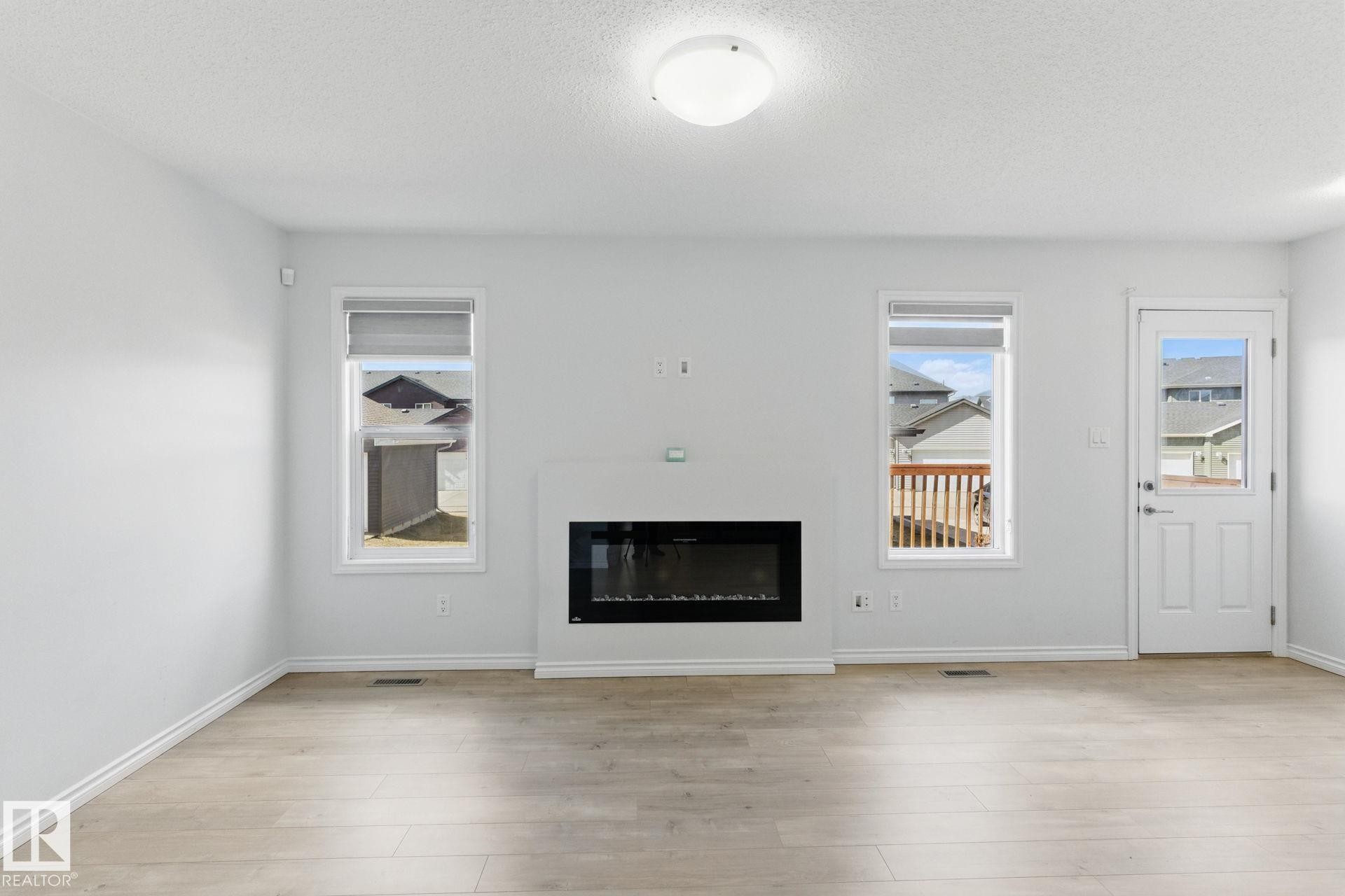 This living space features light-toned flooring, a fireplace, and a door providing exterior access - 2416 Wonnacott Crest Sw, Edmonton, AB - Indoor Photo Showing Living Room With Fireplace
