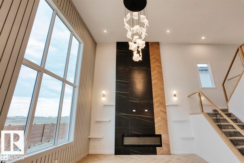 The living area features a fireplace with a black marble and wood accent wall, a grand window providing extensive outdoor views, and a modern chandelier - 63 Jubilation Drive, St. Albert, AB - Indoor Photo Showing Other Room