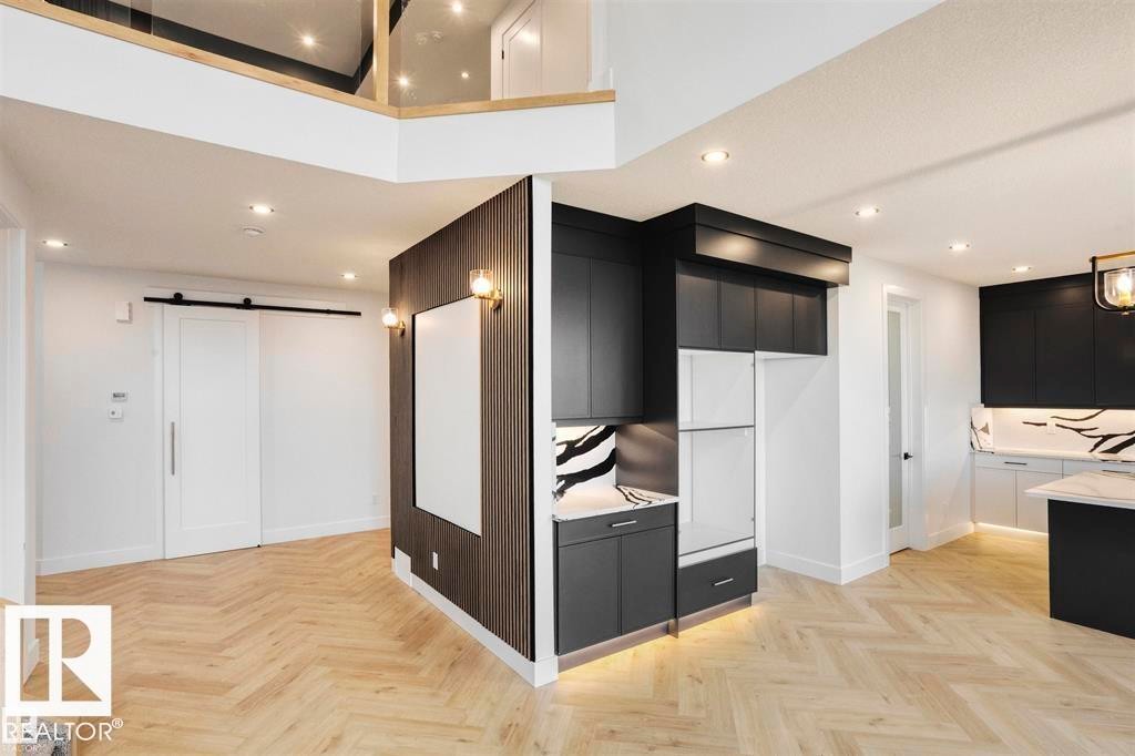 The property features chevron-patterned light wood flooring, recessed lighting, and a modern kitchen with dark cabinetry and light countertops - 63 Jubilation Drive, St. Albert, AB - Indoor Photo Showing Kitchen