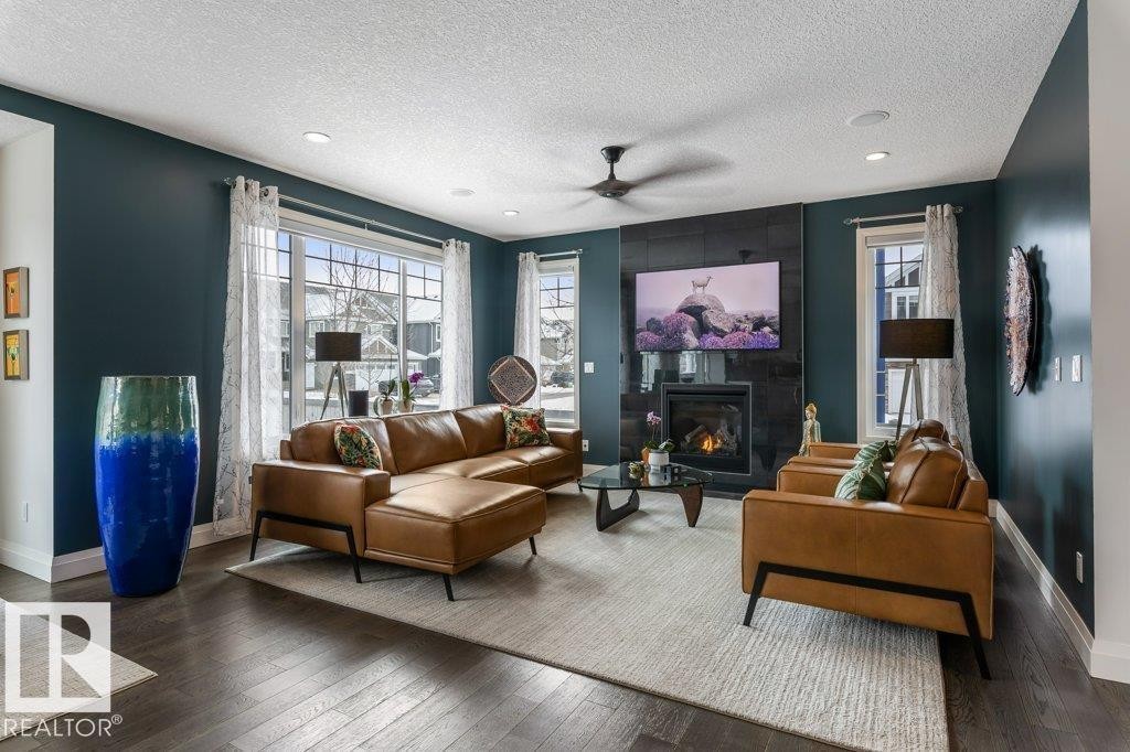 South West Facing Living Room featuring Large Windows, Dark Hard wood Flooring, and Tile Surround Gas Fireplace - 4476 Suzanna Crescent, Edmonton, AB - Indoor Photo Showing Living Room With Fireplace