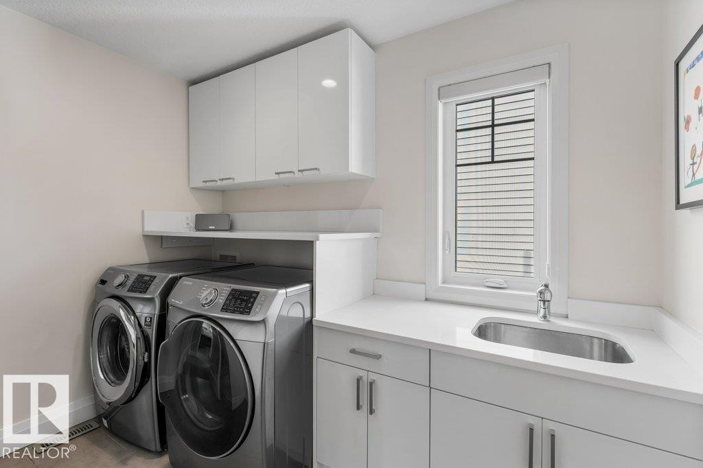 Upstairs Laundry area featuring white cabinetry, a countertop with an integrated sink, and Front Load Washer/Dryer - 4476 Suzanna Crescent, Edmonton, AB - Indoor Photo Showing Laundry Room