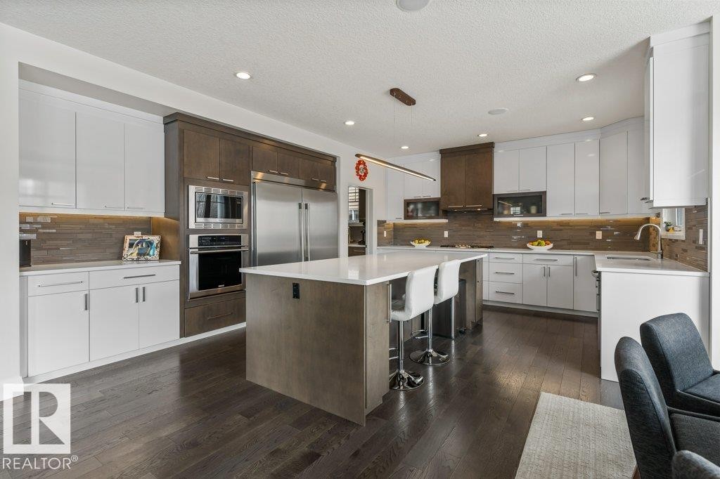 Kitchen Features Dark Hardwood Flooring, Two Tone Kitchen Cabinets, Gas Stove, Wall Oven, and White Quartz Counters - 4476 Suzanna Crescent, Edmonton, AB - Indoor Photo Showing Kitchen With Upgraded Kitchen