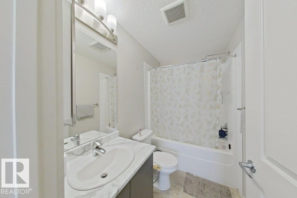 The bathroom features a vanity with a white countertop and an integrated sink, illuminated by an overhead light fixture - 429 390 Windermere Rd, Edmonton, AB - Indoor Photo Showing Bathroom