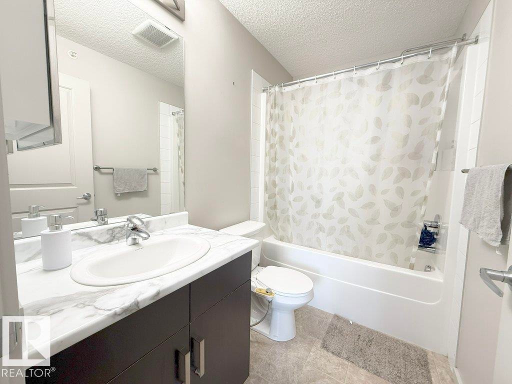 Bathroom featuring a vanity with a white marble-effect countertop and an integrated sink, a large mirror, and a bathtub with a shower - 429 390 Windermere Rd, Edmonton, AB - Indoor Photo Showing Bathroom