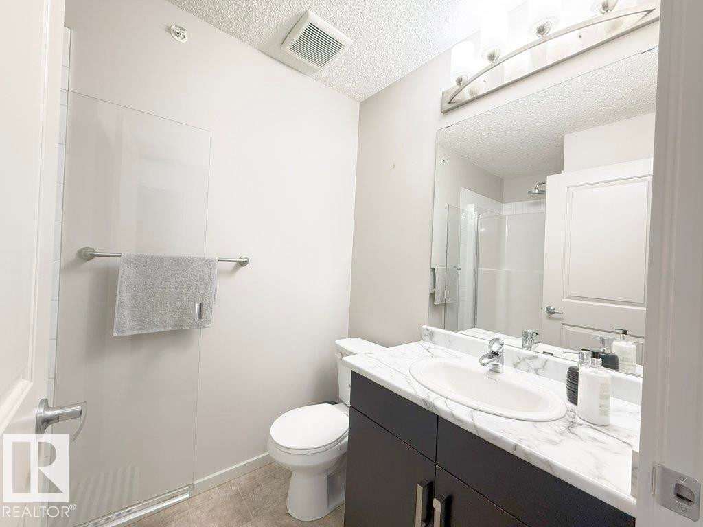 This bathroom features a contemporary vanity with a white marble-patterned countertop, a chrome faucet, and a large mirror - 429 390 Windermere Rd, Edmonton, AB - Indoor Photo Showing Bathroom