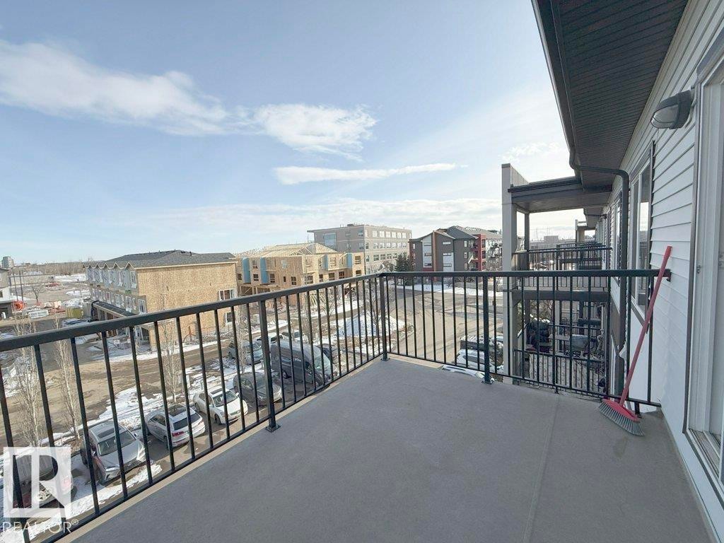 The property features a balcony with a black metal railing, offering views of the surrounding buildings and outdoor parking area - 429 390 Windermere Rd, Edmonton, AB - Outdoor With Balcony