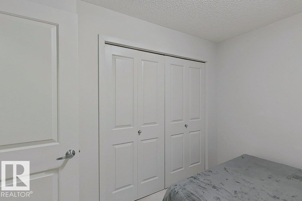 This room features white walls, a white door with a brushed nickel handle, and a closet with white bi-fold doors - 429 390 Windermere Rd, Edmonton, AB - Indoor Photo Showing Bedroom
