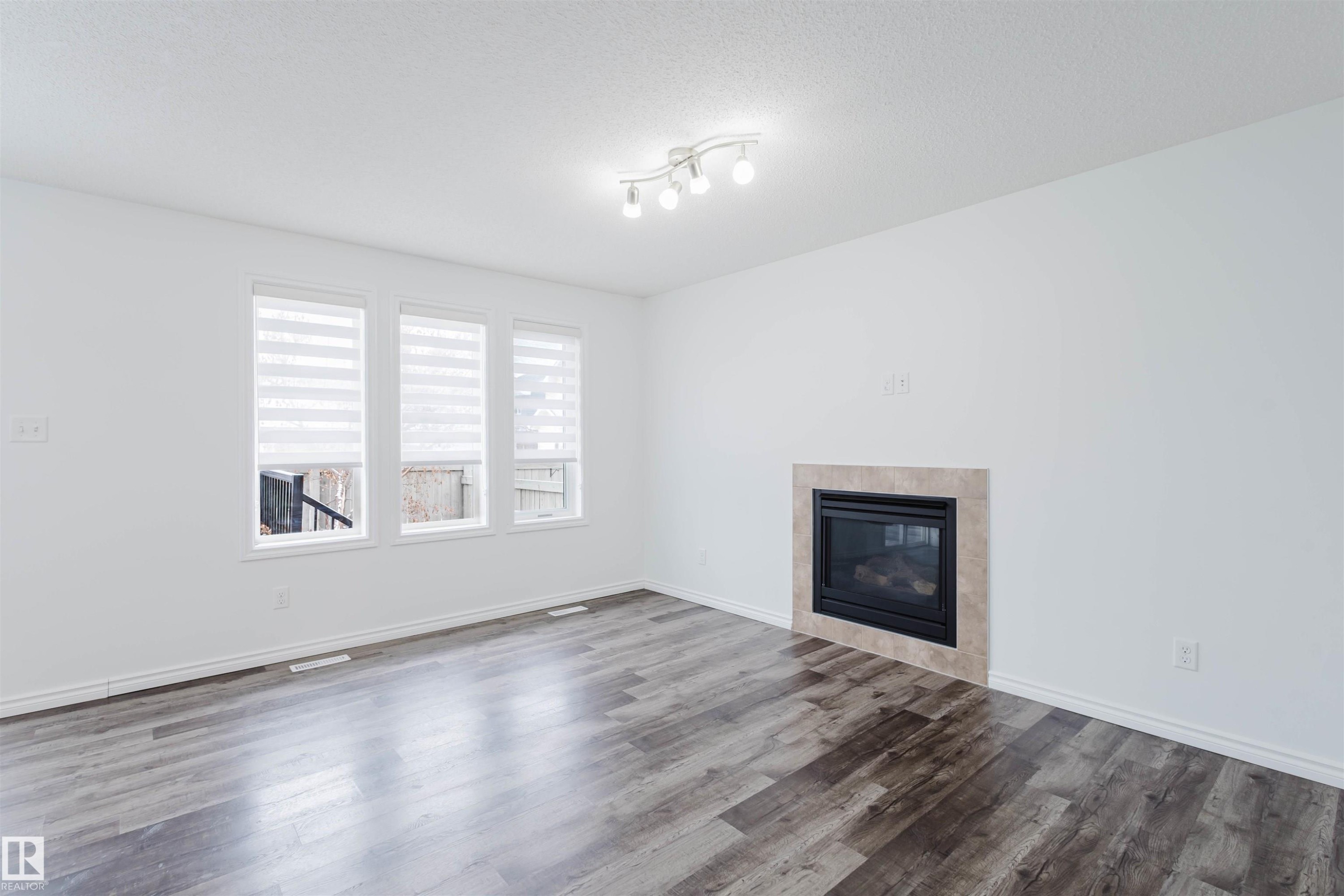 Unfurnished living room featuring a tile fireplace, a textured ceiling, and dark wood-type flooring - Edmonton, AB - Indoor Photo Showing Living Room With Fireplace