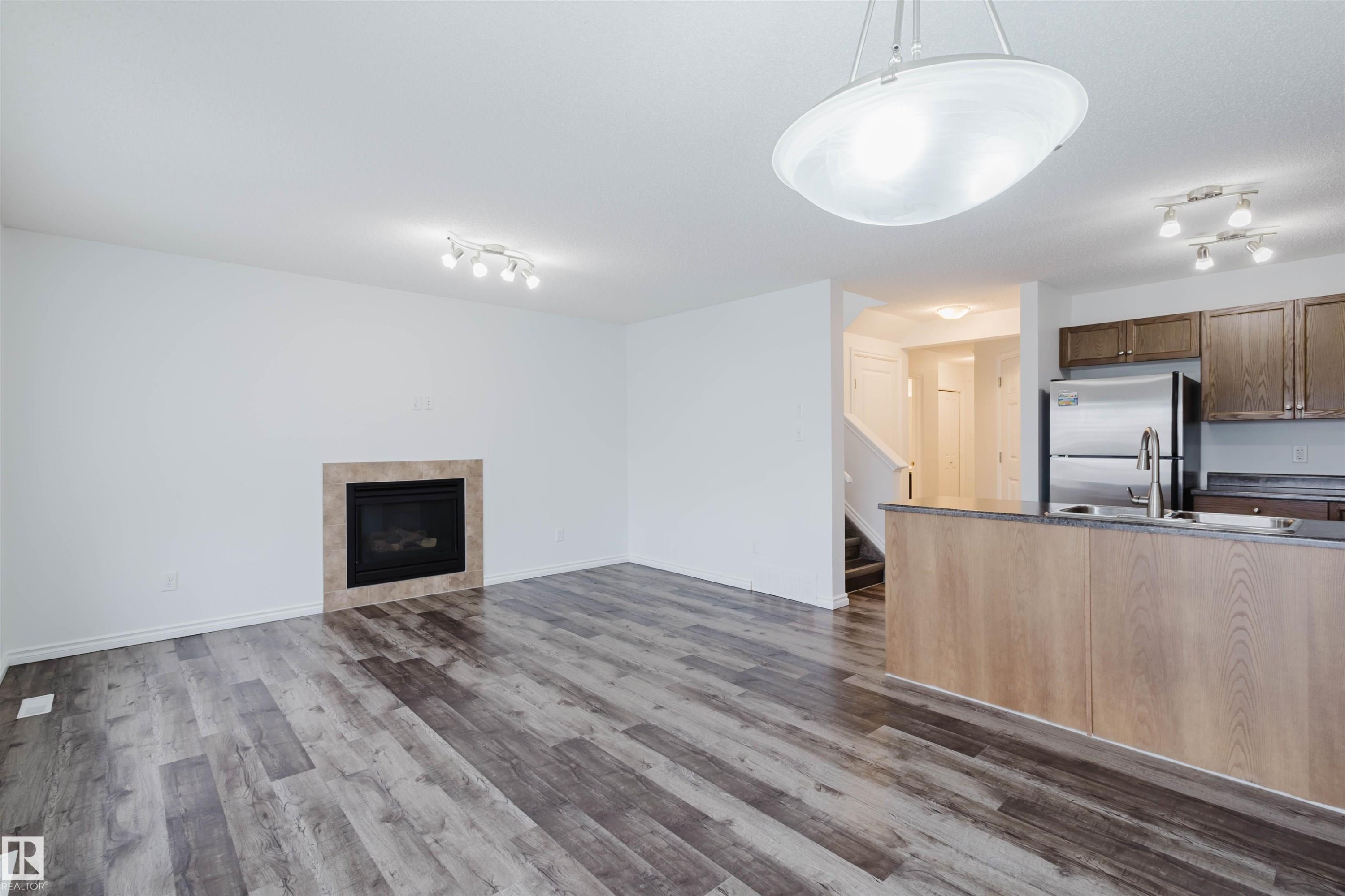 Unfurnished living room featuring rail lighting, a tile fireplace, and dark wood-style floors - Edmonton, AB - Indoor With Fireplace